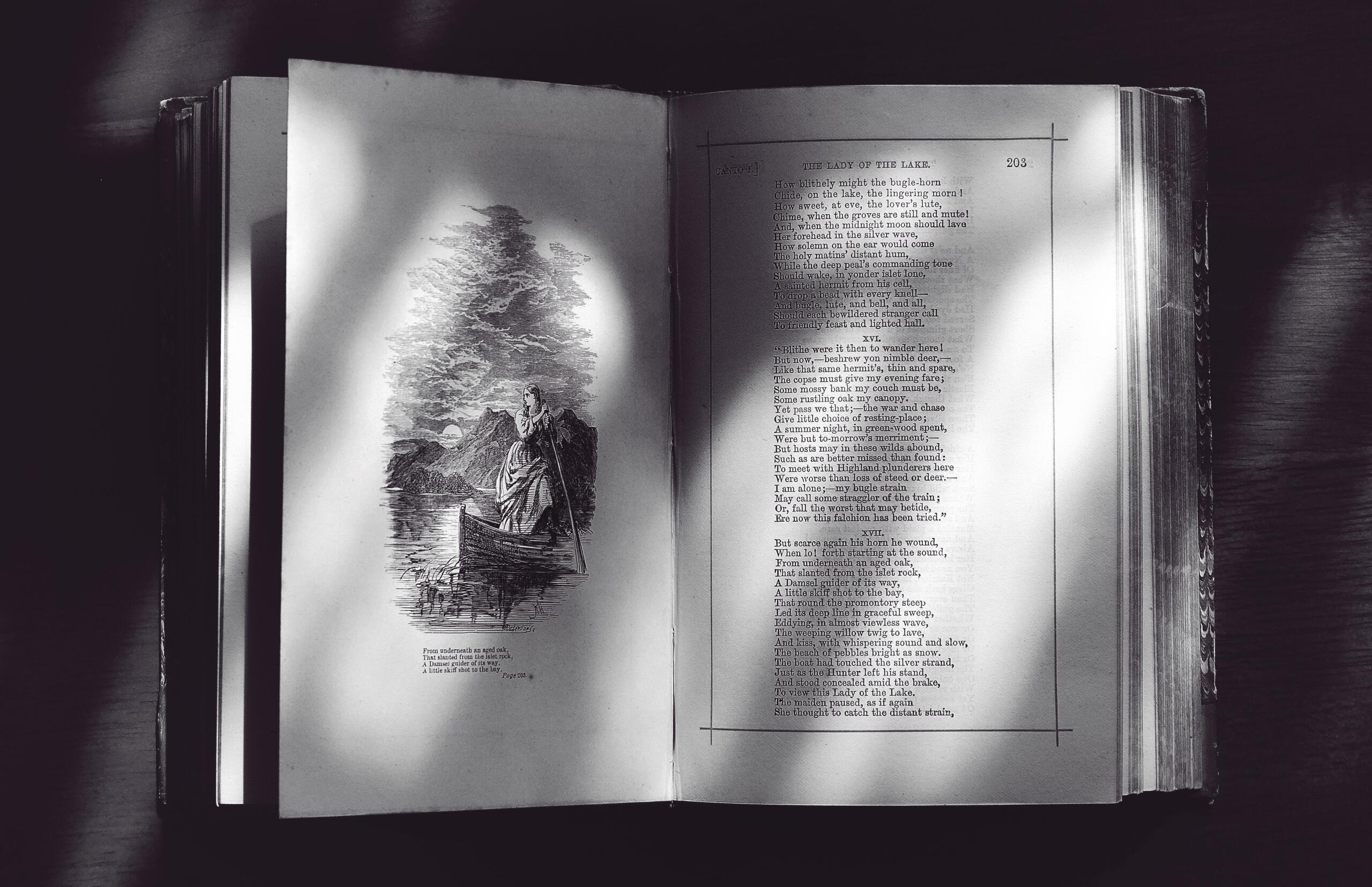 A black-and-white image of an open poetry book resting on a flat surface, highlighting the printed poems and timeless feel of the pages. Source: Suzy Hazelwood.