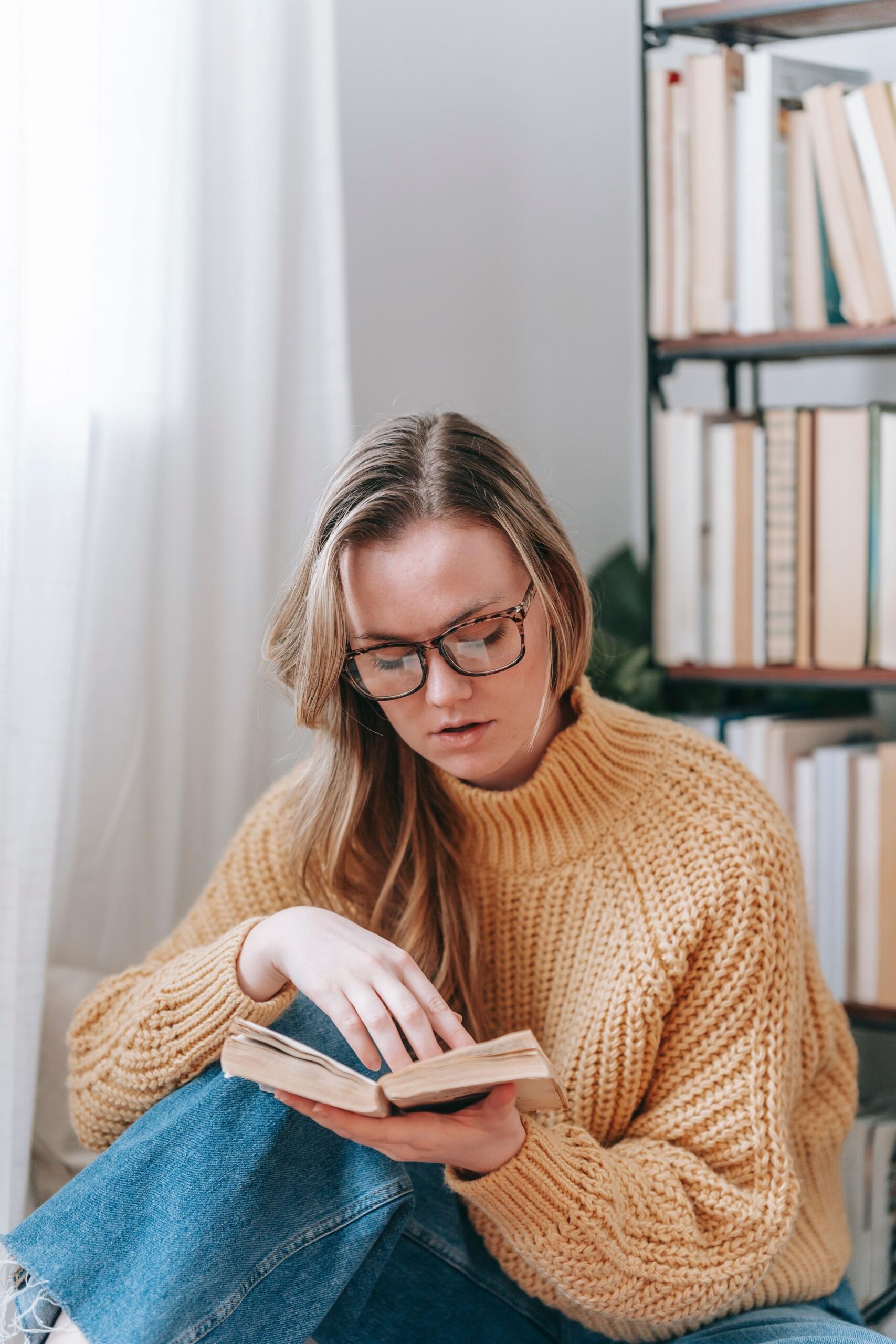A woman reading a book while seated in a cozy space, focused on the pages and enjoying a quiet moment of reflection.