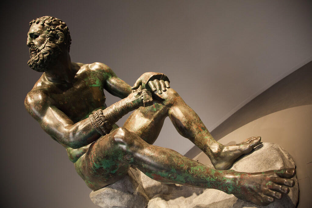 Ancient Greek bronze sculpture of the Seated Boxer, portraying a weary athlete after combat.
