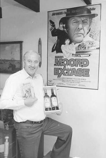 A.C. Baantjer, Dutch crime writer, posing with books and wine bottles in front of a Moord in Extase movie poster.