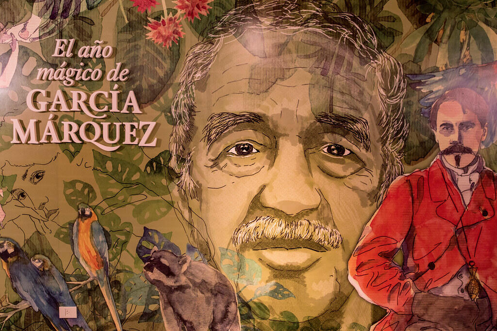 Illustrated mural celebrating Colombian Nobel Prize-winning author Gabriel García Márquez. The artwork features a large portrait of García Márquez surrounded by tropical plants, colorful birds, monkeys, and a figure representing one of his literary characters, reflecting the magical realism of his novels.