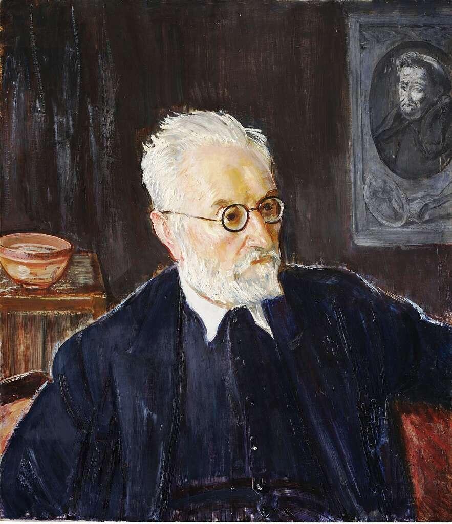 Portrait of Spanish philosopher, writer, and educator Miguel de Unamuno, painted by Ignacio Zuloaga. Unamuno is depicted with white hair, a beard, and round glasses, wearing a dark suit while seated indoors. A framed portrait hangs in the background, emphasizing his intellectual legacy.