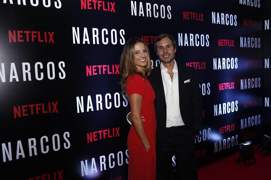 Two people posing on the red carpet at a Netflix Narcos event with a branded backdrop.