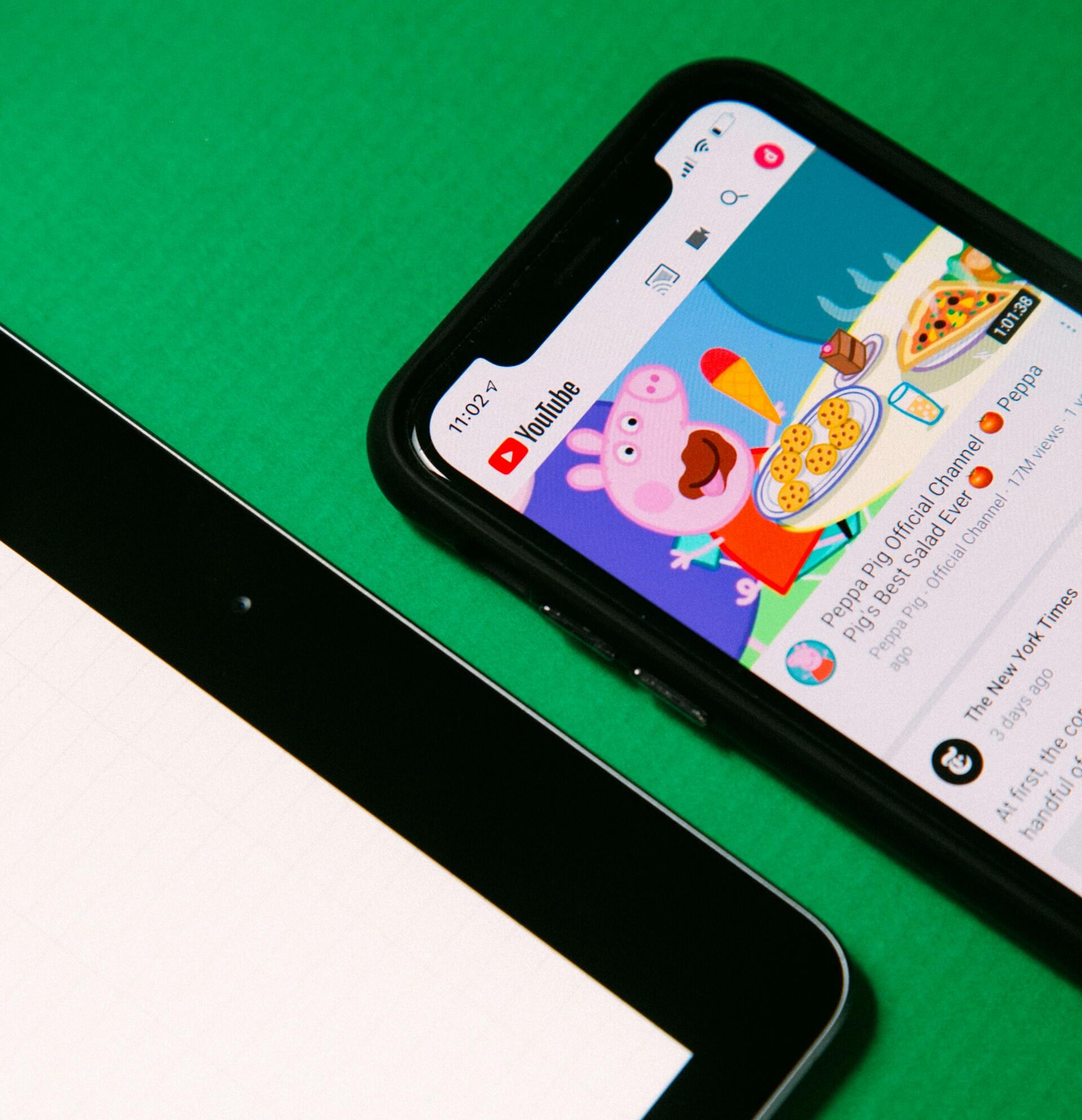 Smartphone displaying a Peppa Pig YouTube video next to a tablet on a green background.