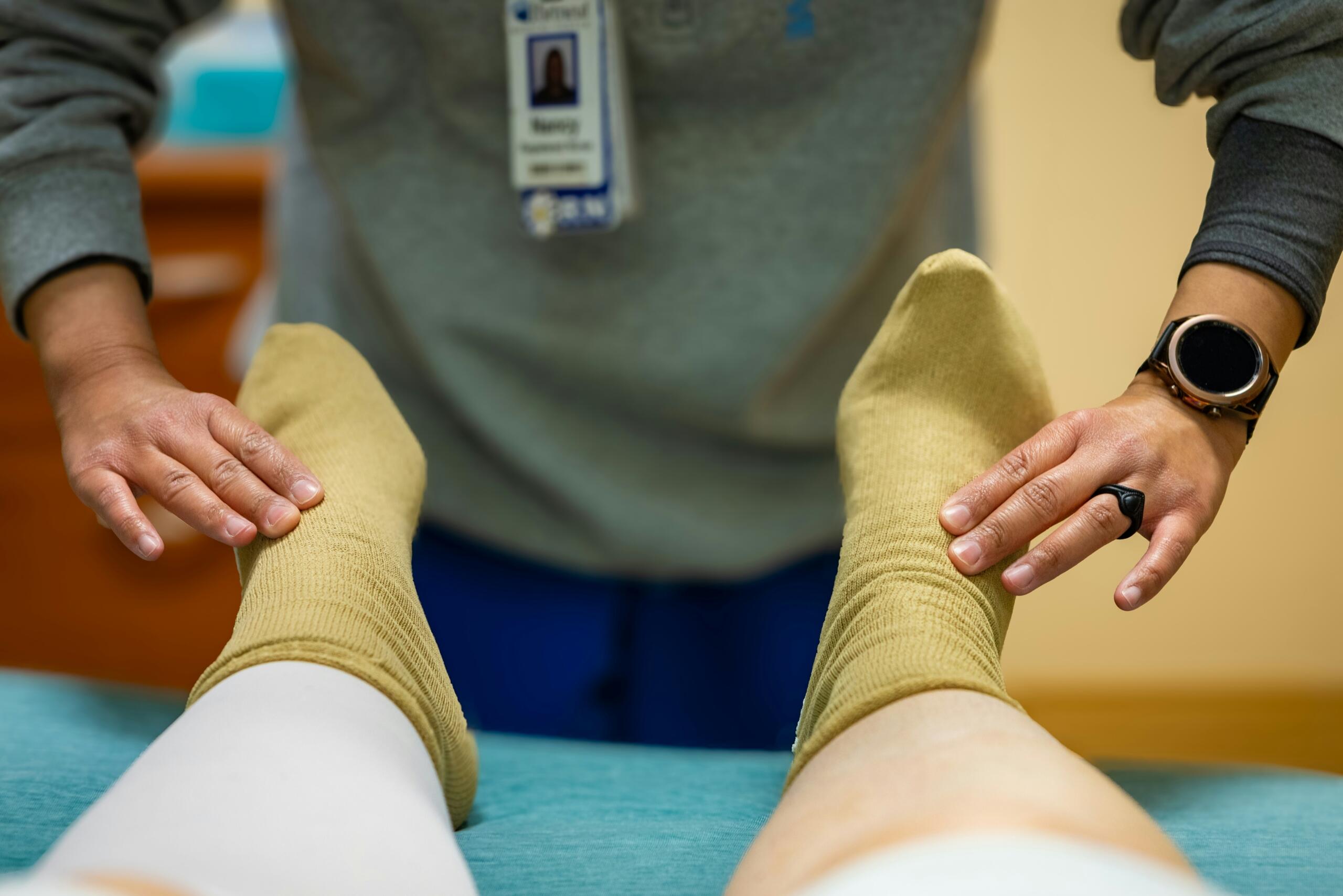 Healthcare professional checks patient's feet wearing yellow socks while standing by a medical bed.