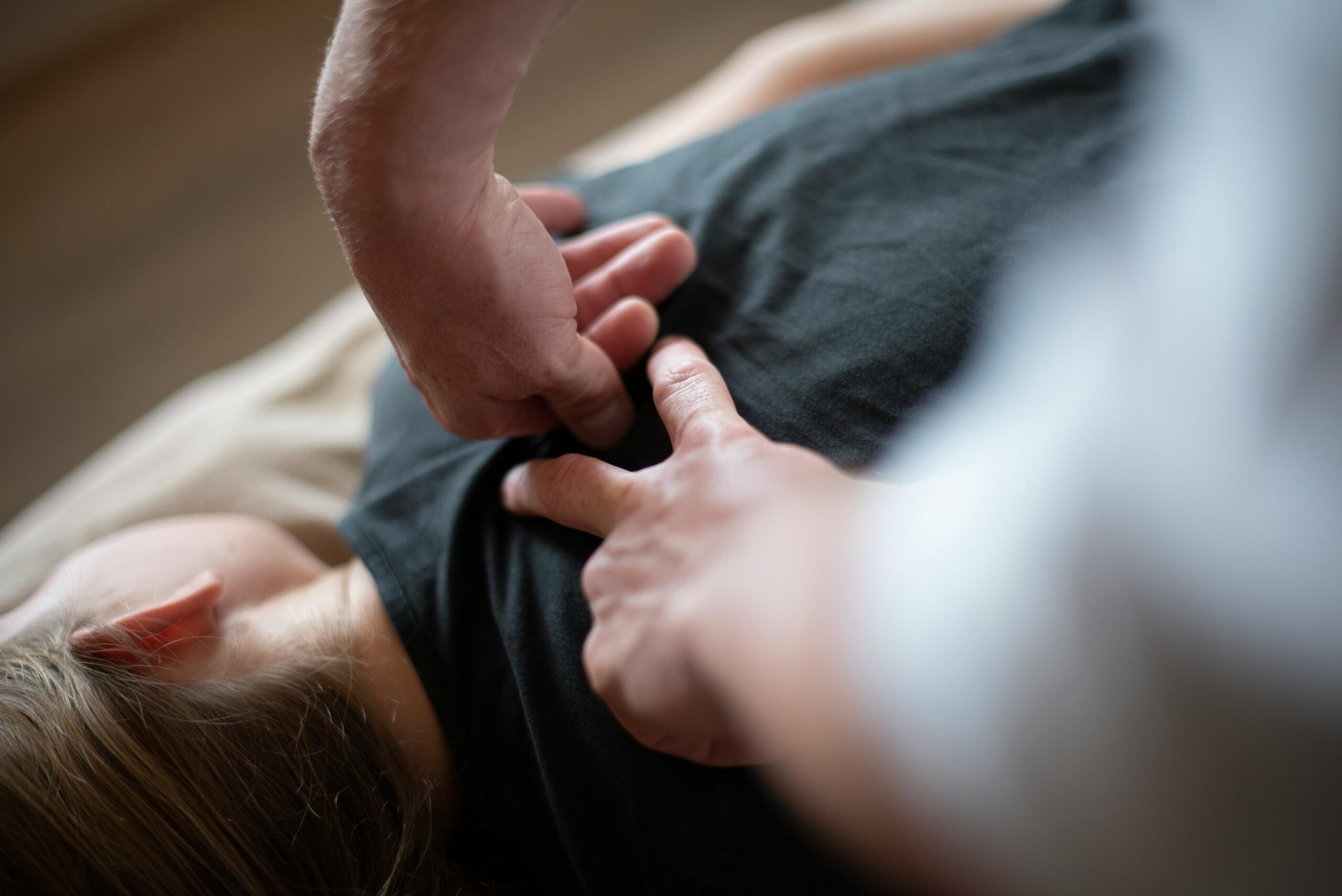 A person lying face down on a massage table, receiving a back massage from a therapist.