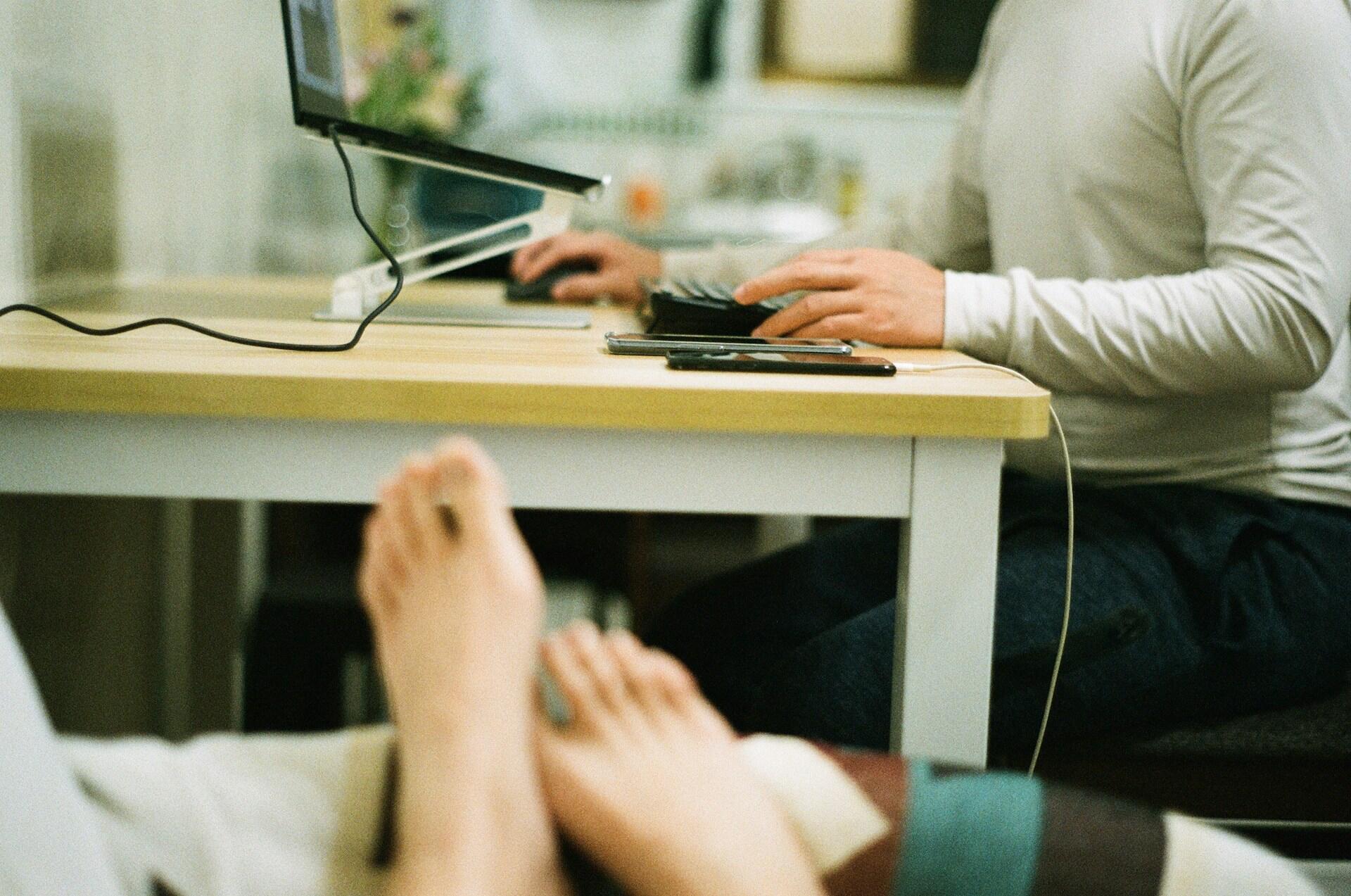 A man at a desk using a computer, with another person seated beside him, engaged in conversation.