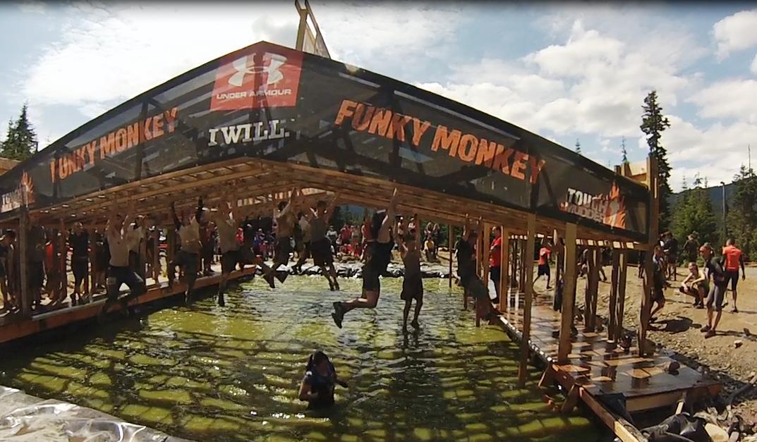 The Funky Monkey event banner at a Tough Mudder event. Athletes are in front, enjoying the fitness activities.
