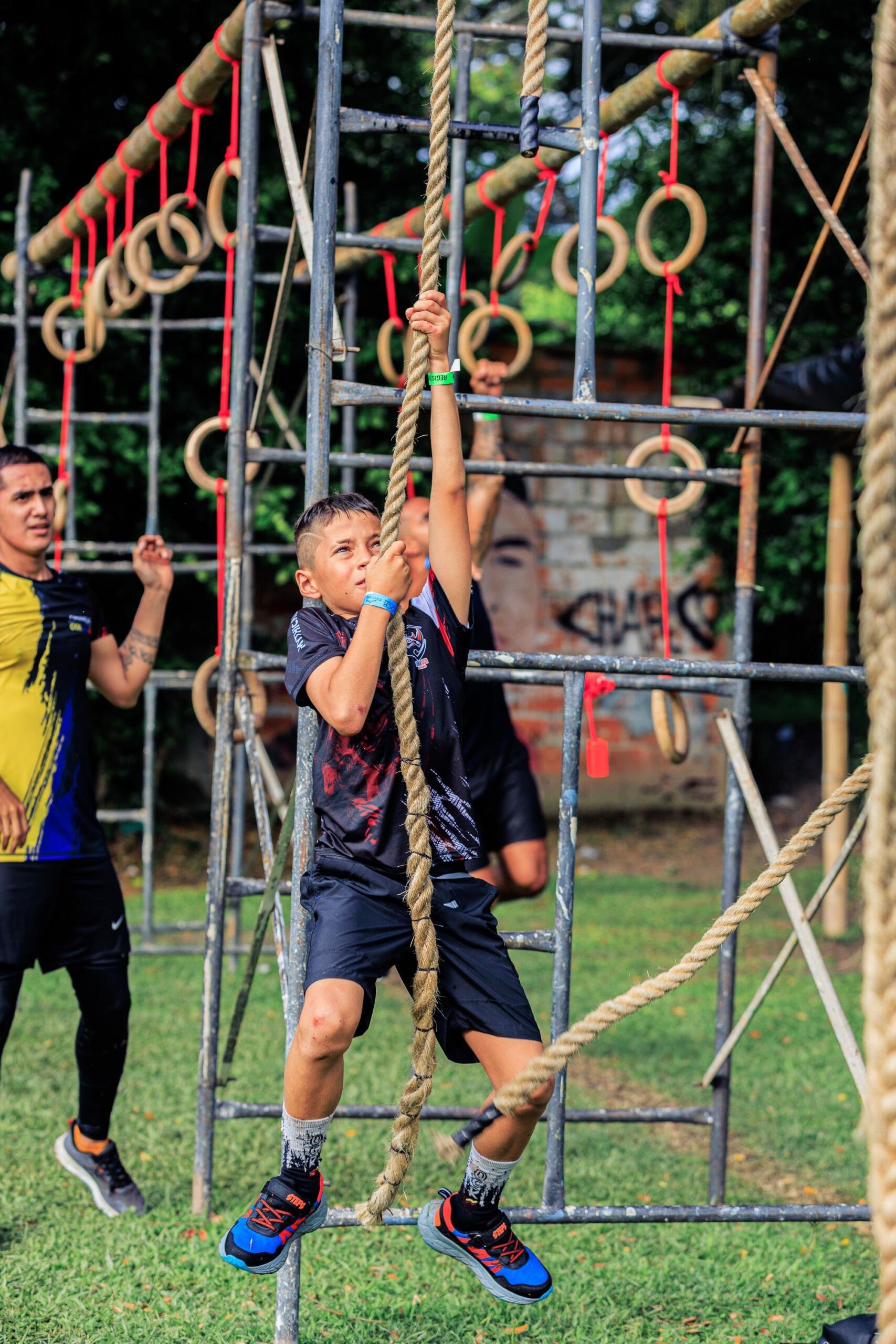 A boy climbs ropes at an obstacle course competition, determination on his face.