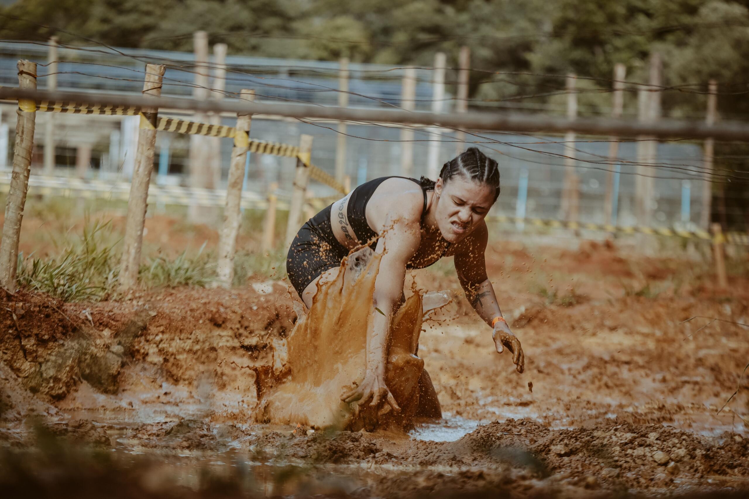 A woman athlete fights through mud in an obstacle course competition, determination on her face.