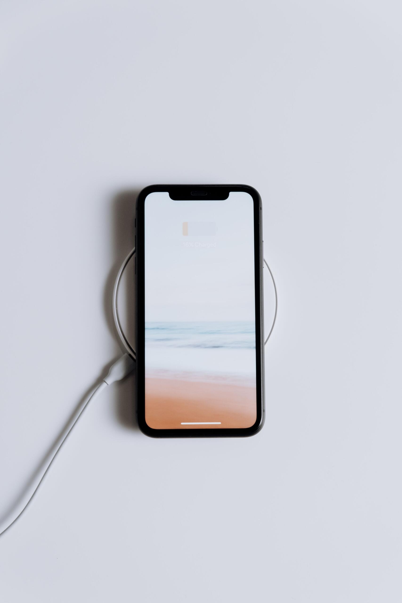 An overhead shot of a sleek, white wireless charging pad resting on a desk. A modern smartphone sits centered on the pad.