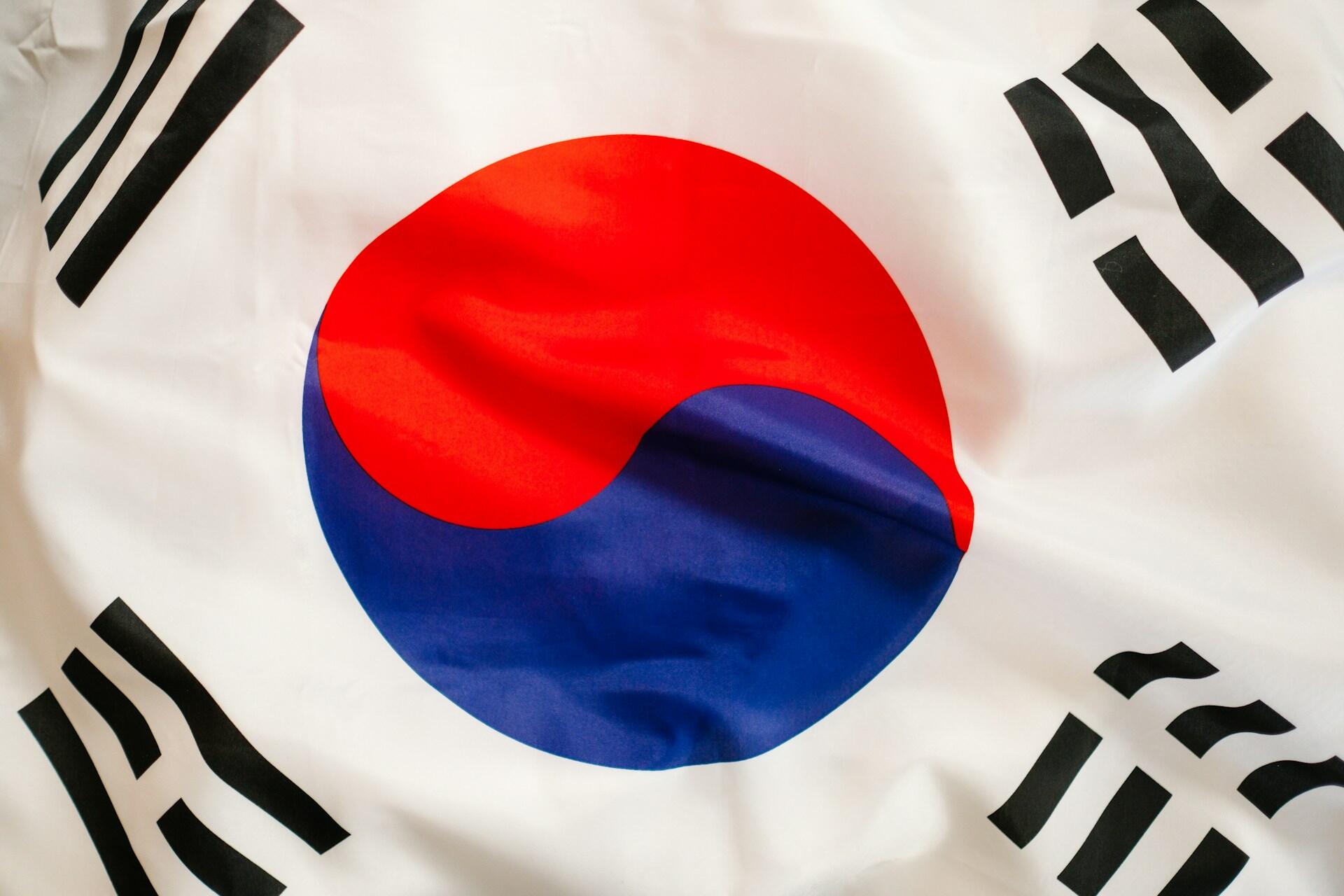 Waving South Korean flag featuring a red and blue yin-yang symbol and four black trigrams on a white background.