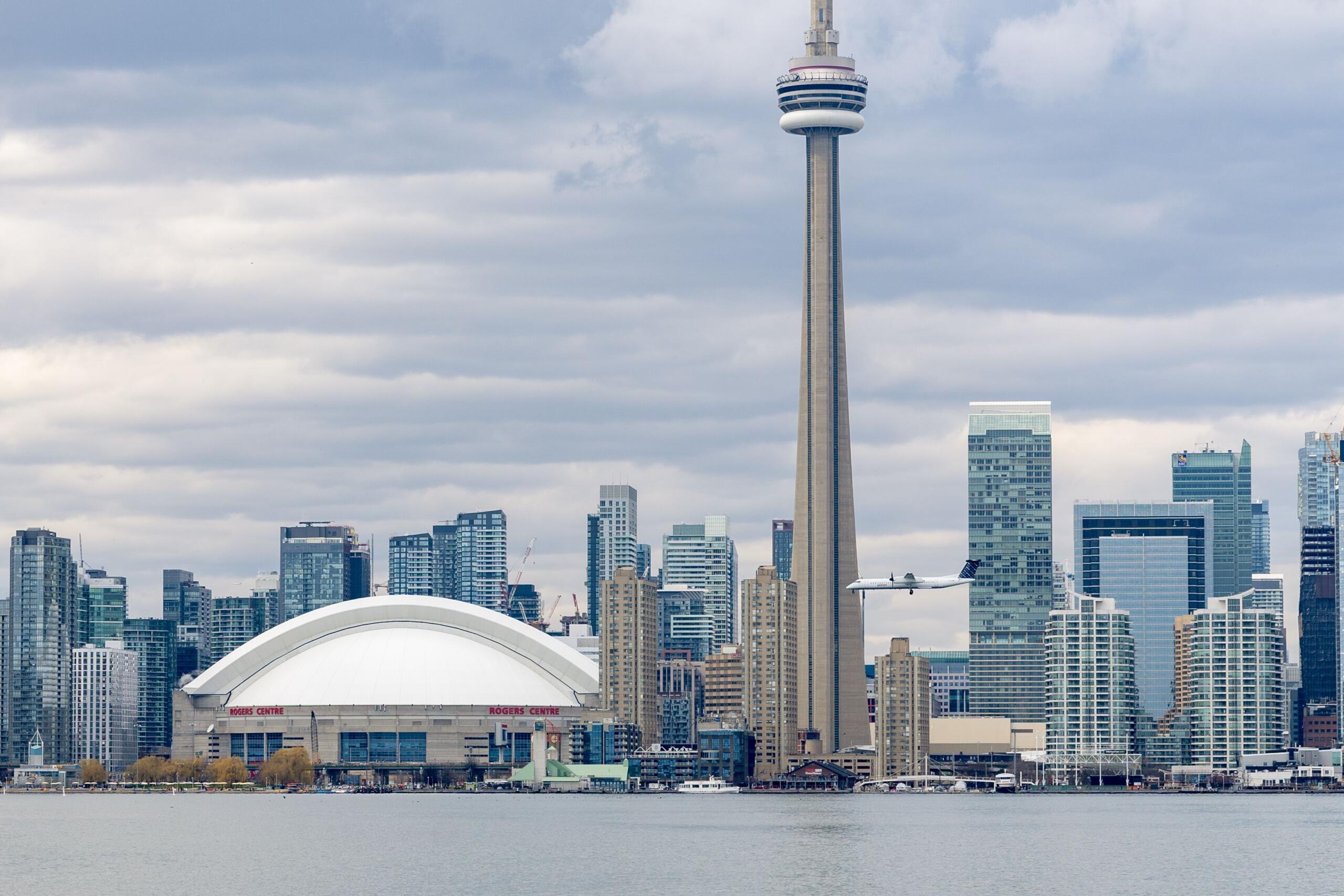 A passenger plane descends toward Billy Bishop Toronto City Airport, approaching the runway beside Toronto's waterfront with the city skyline visible in the background.