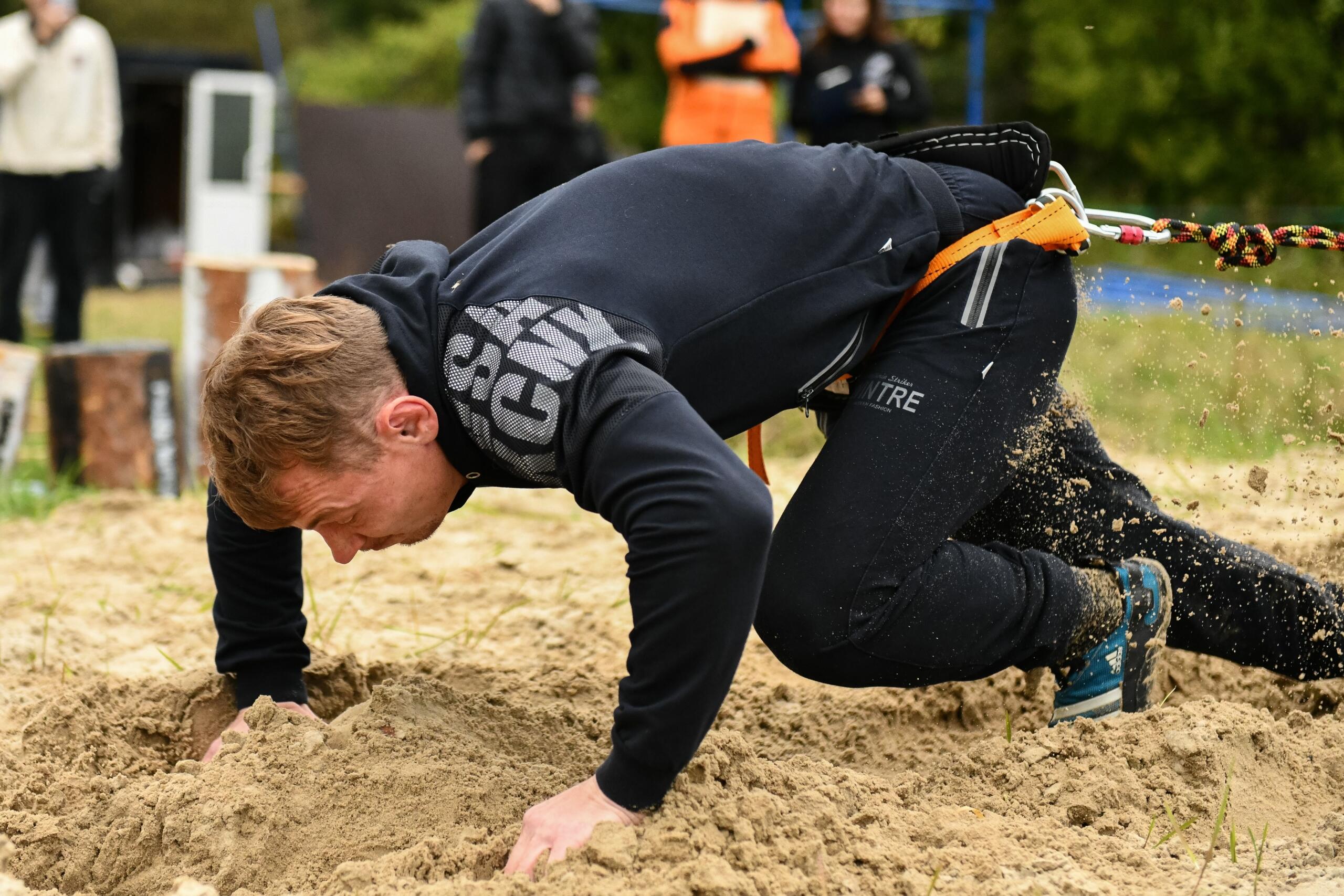 A man trains in a sandy obstacle course, powering through a challenging section while building strength, agility, and endurance outdoors.