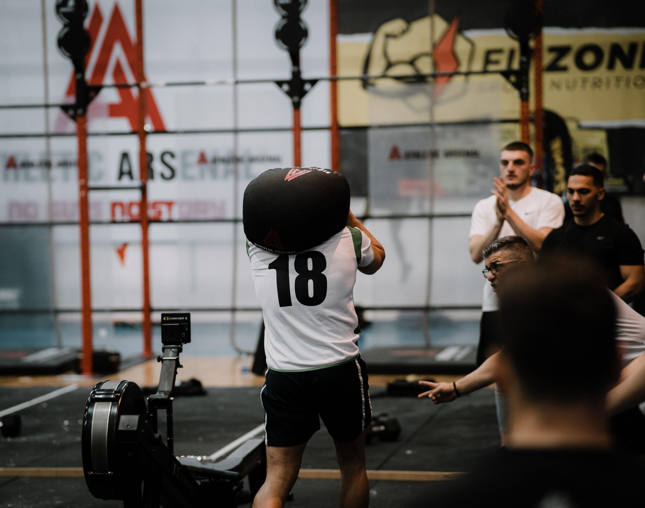 A man carries a heavy sandbag during a functional fitness workout, holding it securely across his shoulders as he trains for strength and endurance.