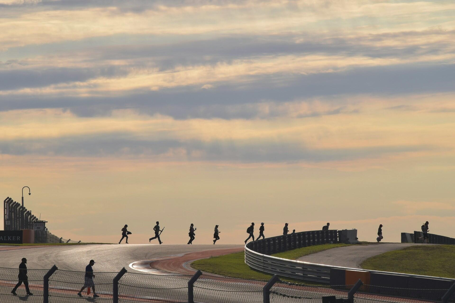 Silhouettes of people walking and running along a race track at sunset with a cloudy sky in the background.