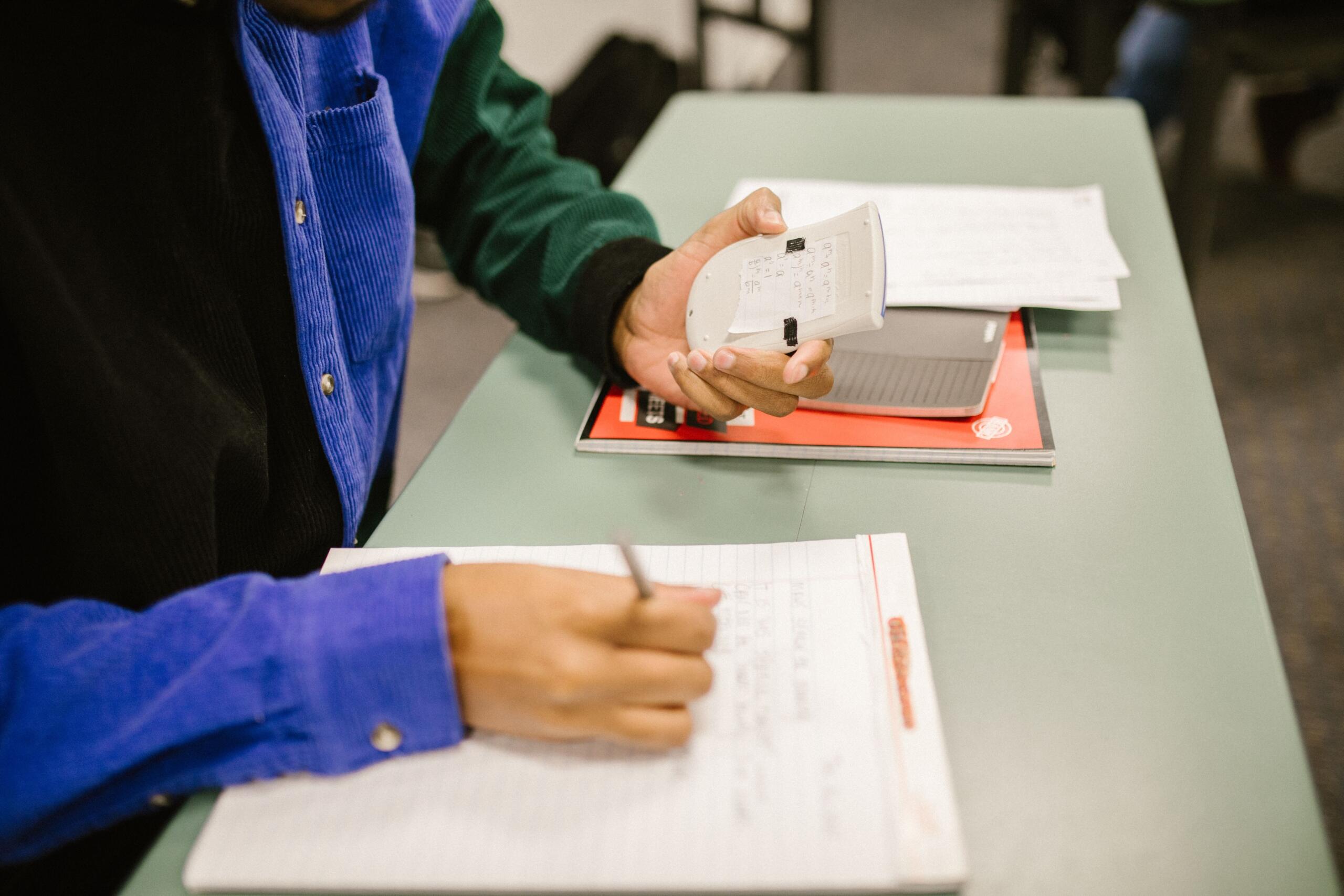 a student writes in a workbook or application page to enter university. They write on the page while holding a calculator.