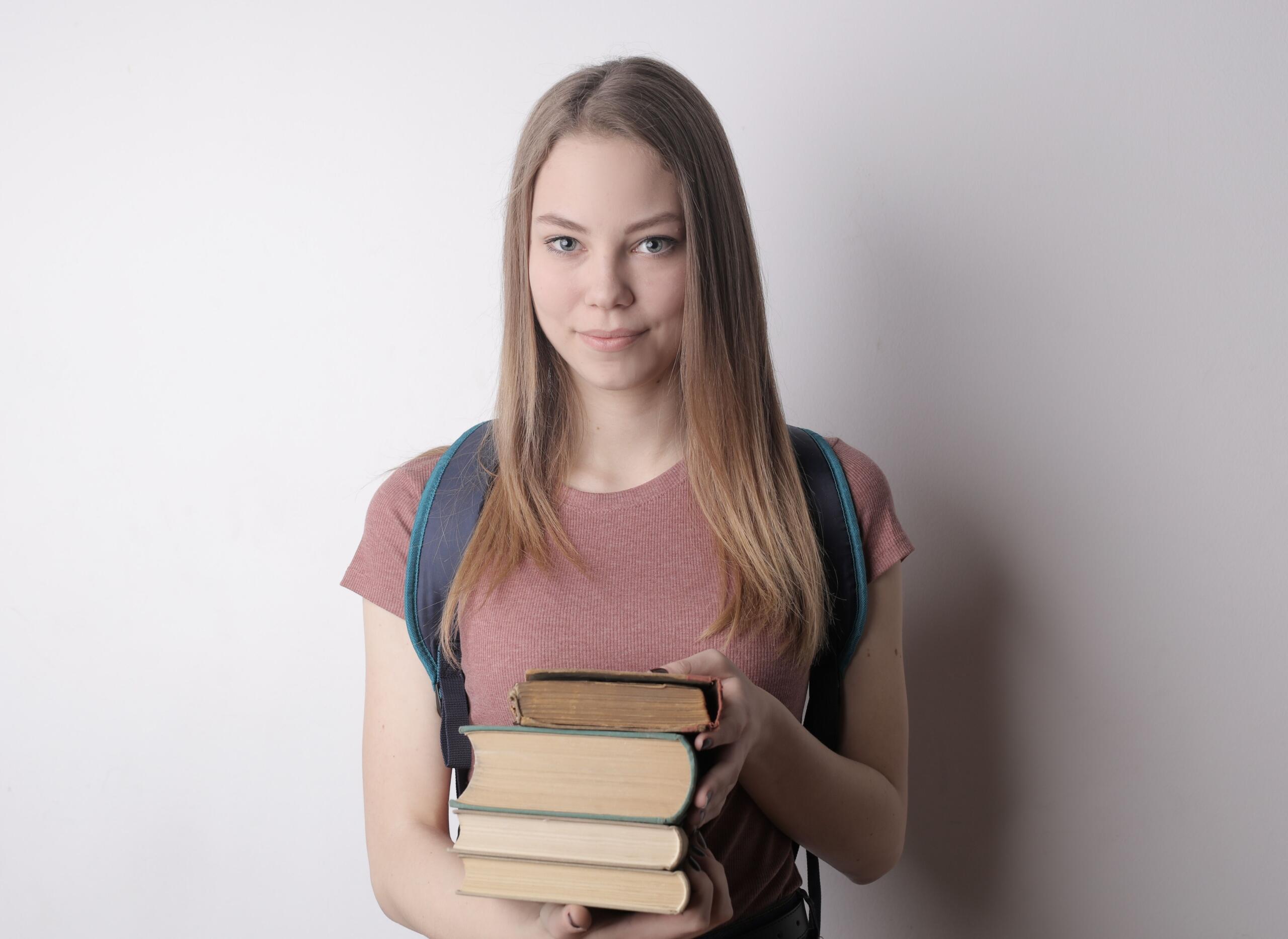 A grade 12 student stands smiling, holding a heavy load of books.