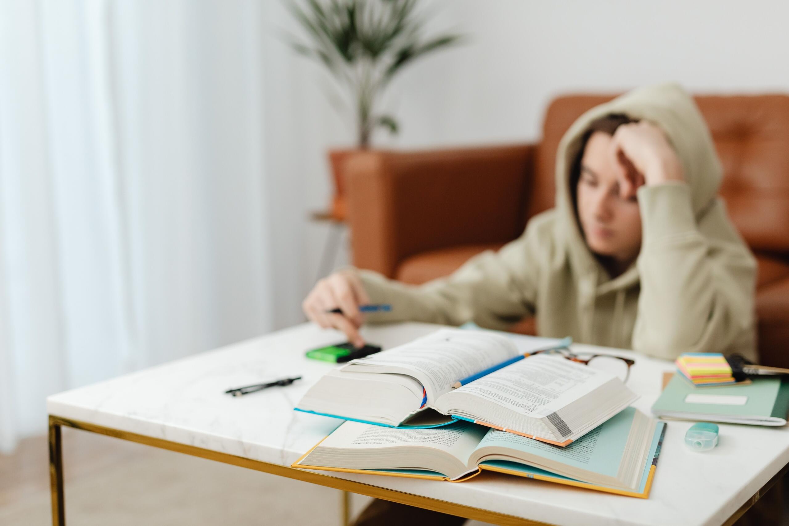 A student wears his hood up, reviewing notes for the diploma exam. He works at home, in front of a couch.