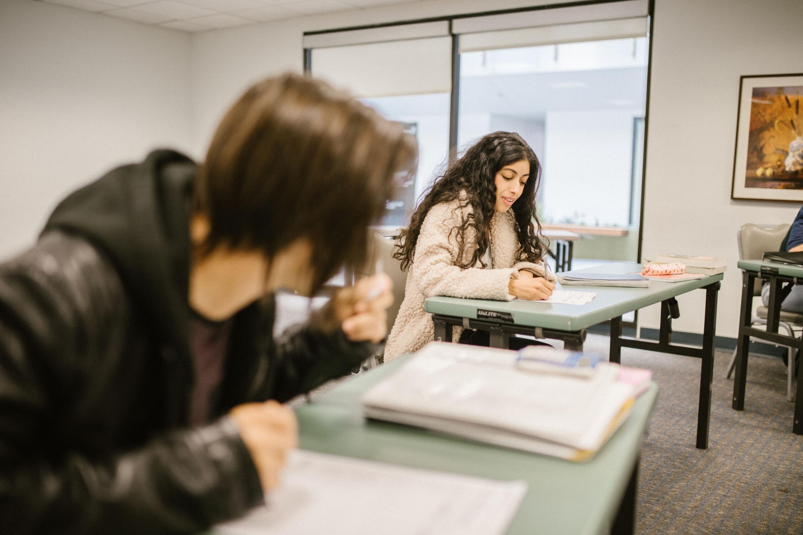 two teenage girls complete literacy activities in a classroom.