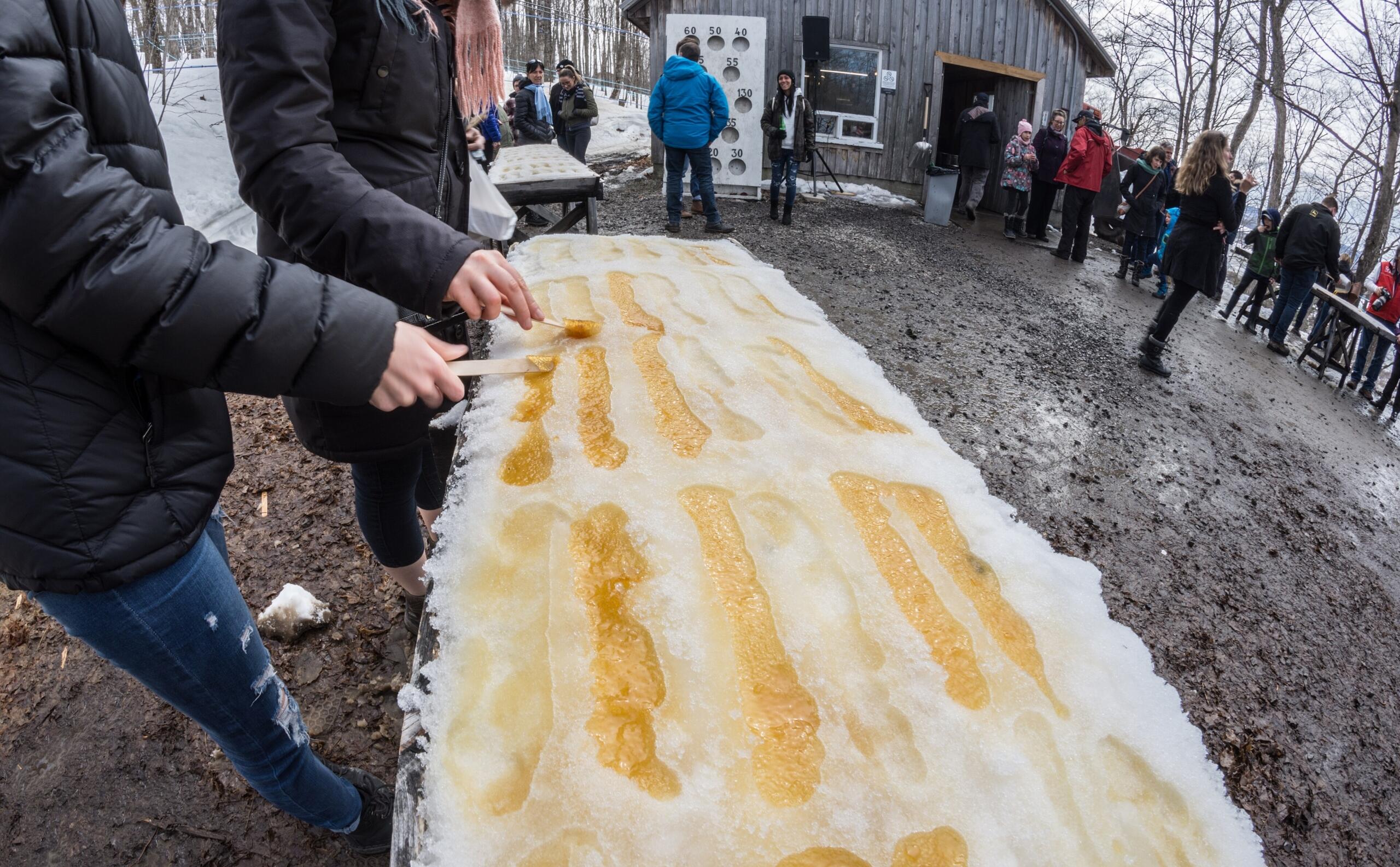 People enjoying traditional maple taffy on snow outdoors at a rustic sugar shack during winter.