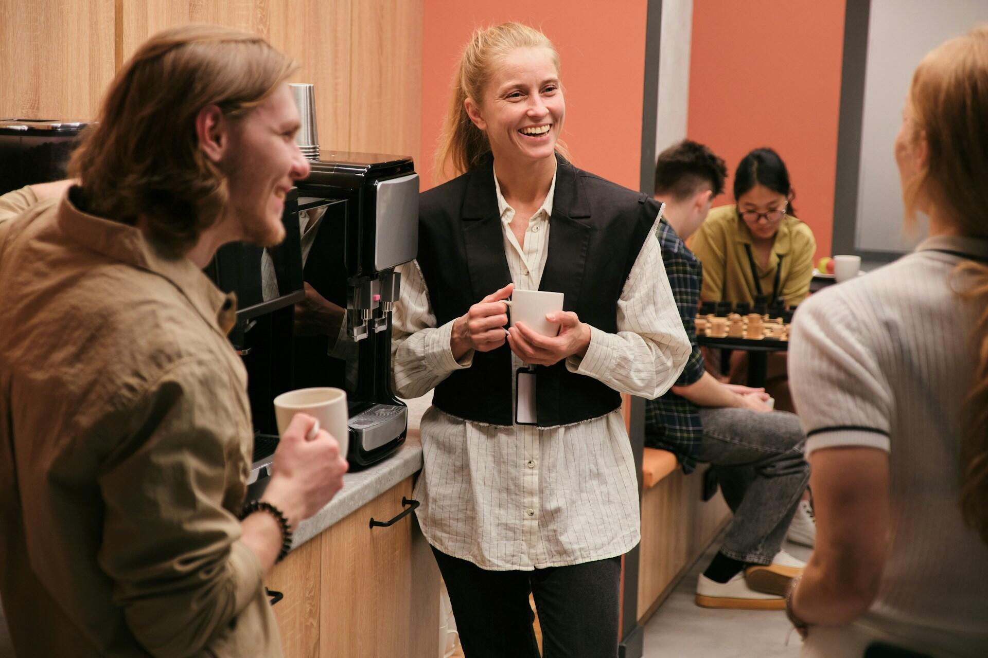 a group of people in an office break room enjoying coffee and chatting and laughing together