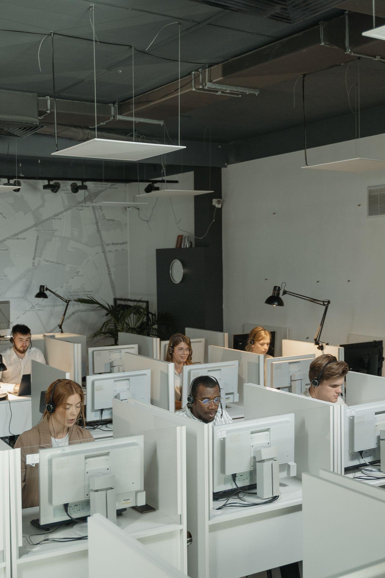 room of people using computers at cubicles, wearing headset headphones and microphones