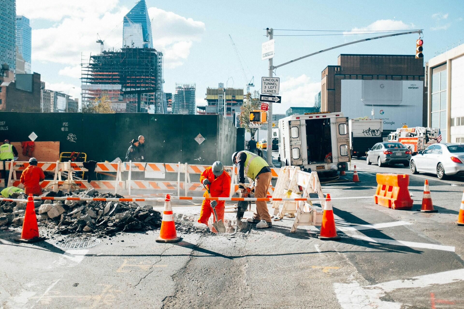 construction workers drilling into the road with lots of orange cones and other safety measures in place nearby