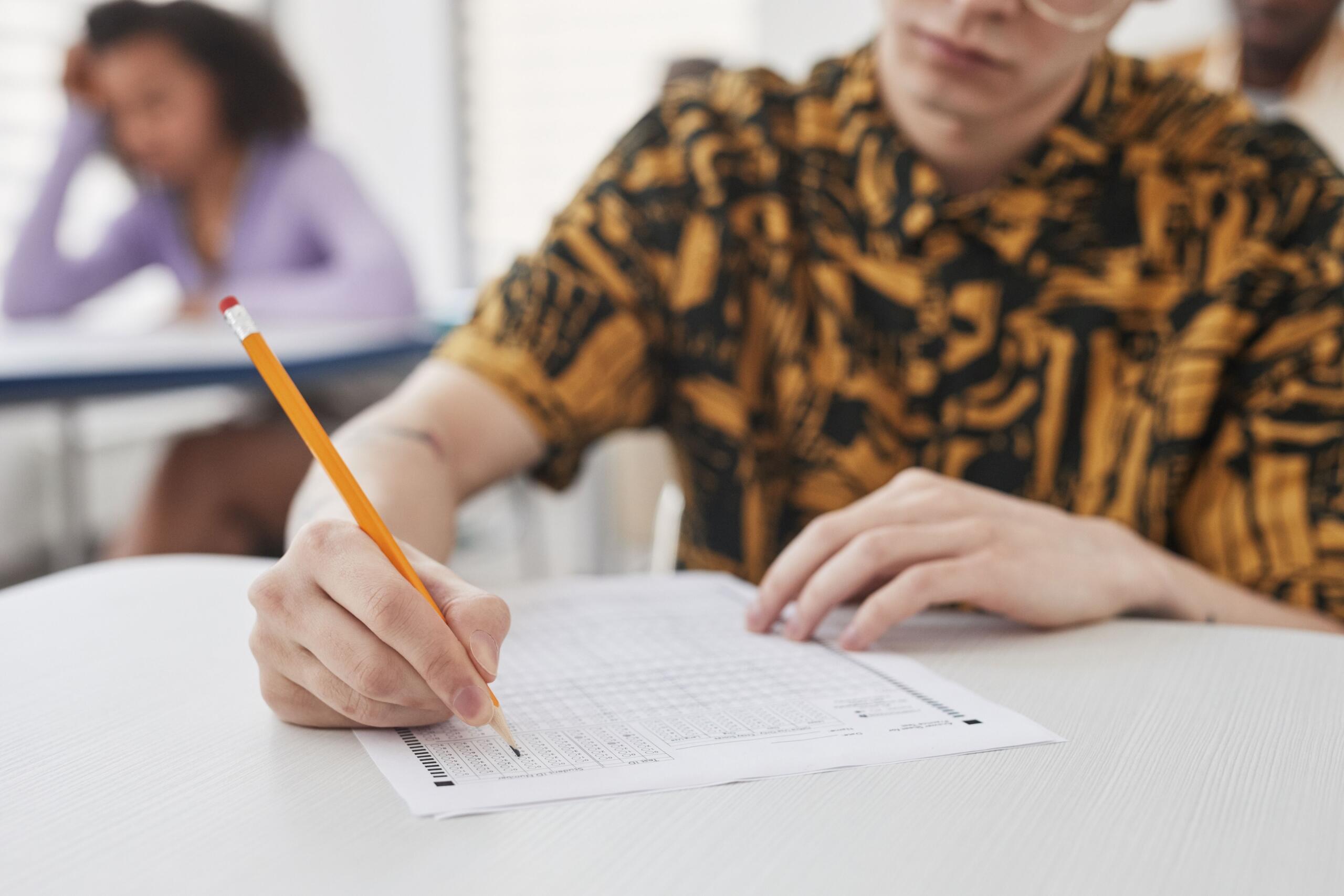 a student writes an exam, his pencil writing intently on the page.