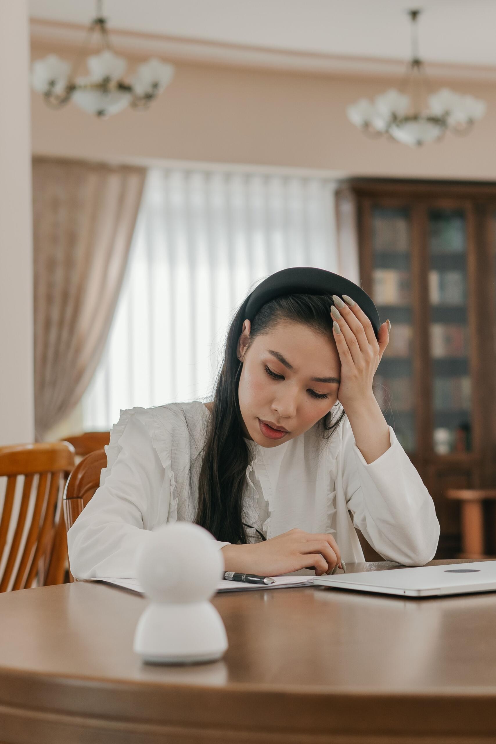 a young woman studies at a dining room table looking stressed.