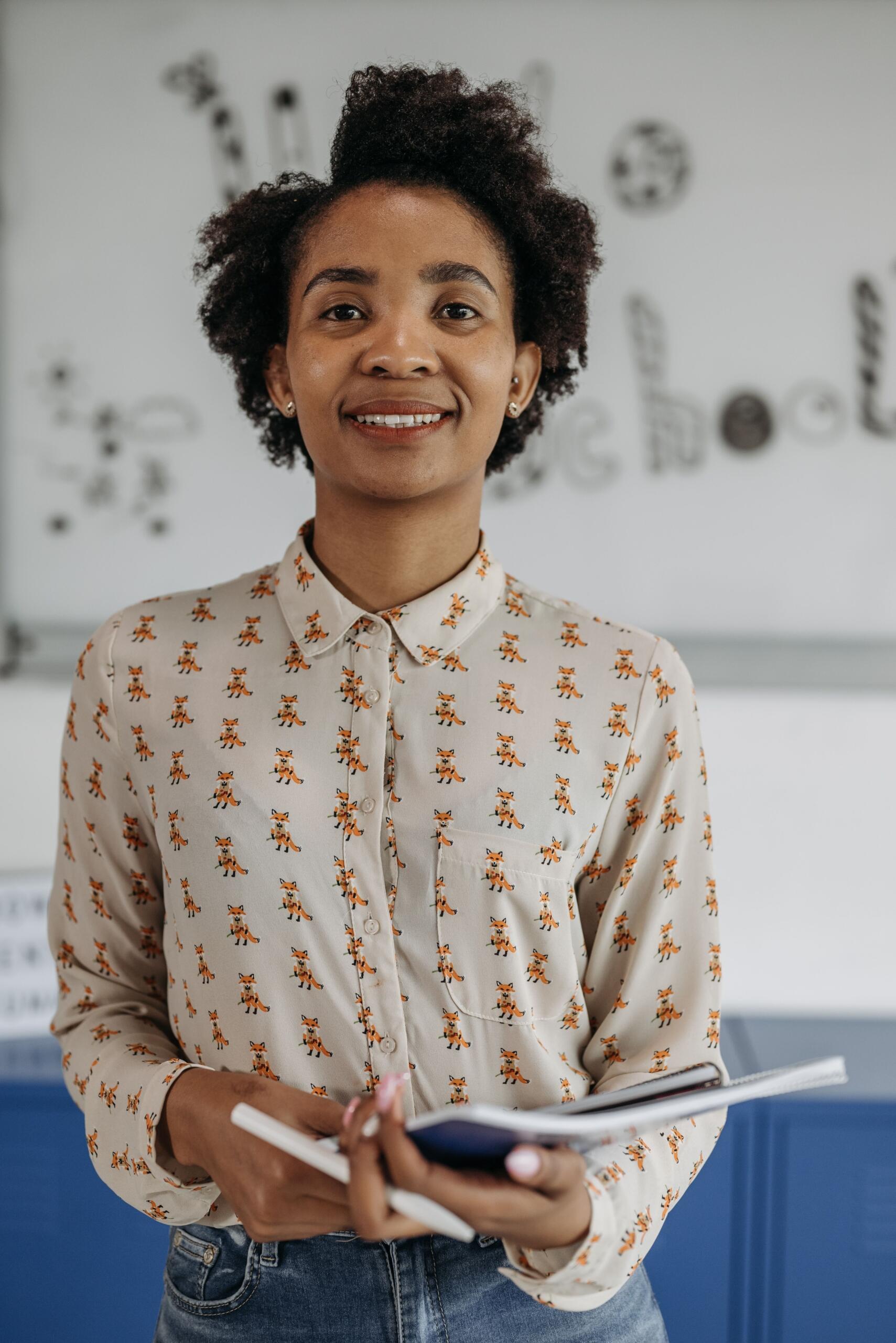 A teacher smiles, holding notebooks and a pen. Source: Pavel Danilyuk.