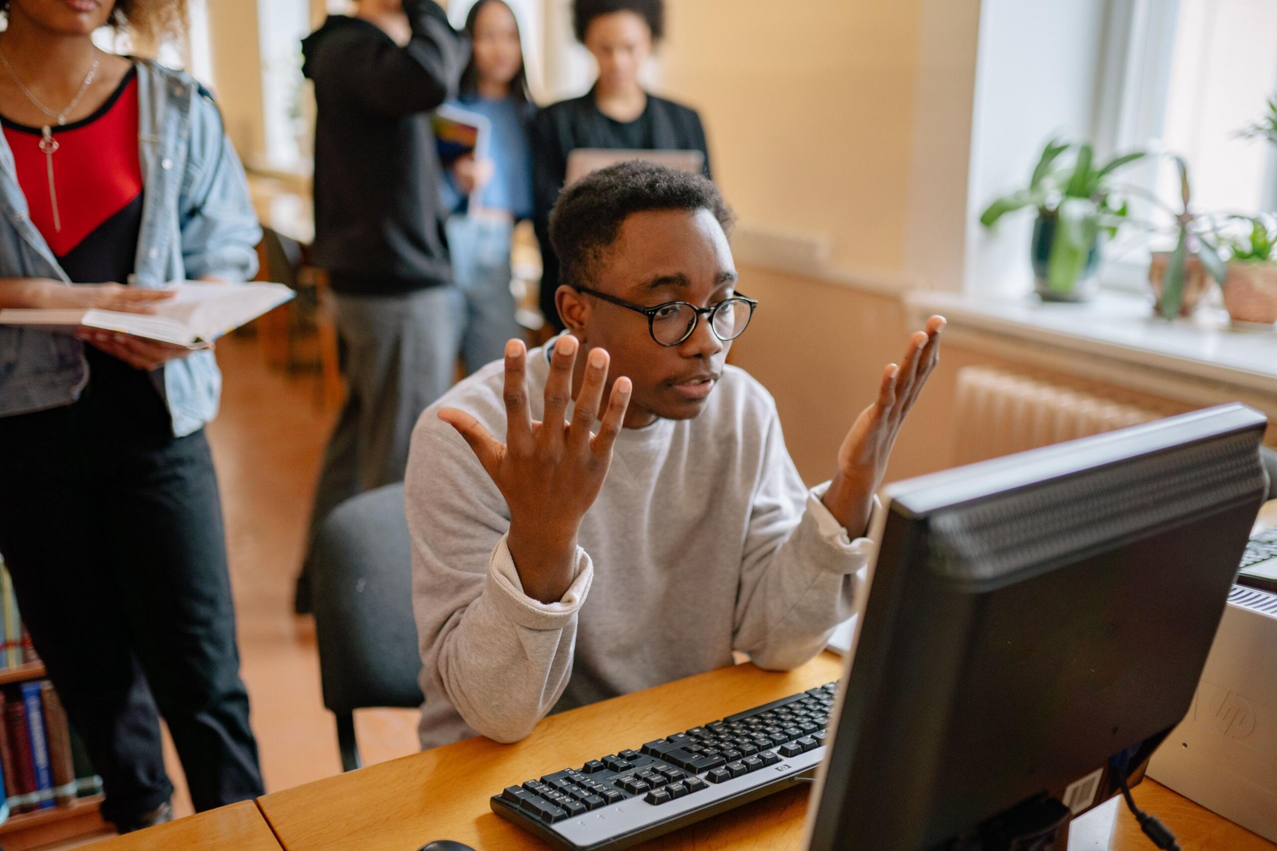 A student sits in front of a computer, appearing shocked and distressed at news he as just heard.