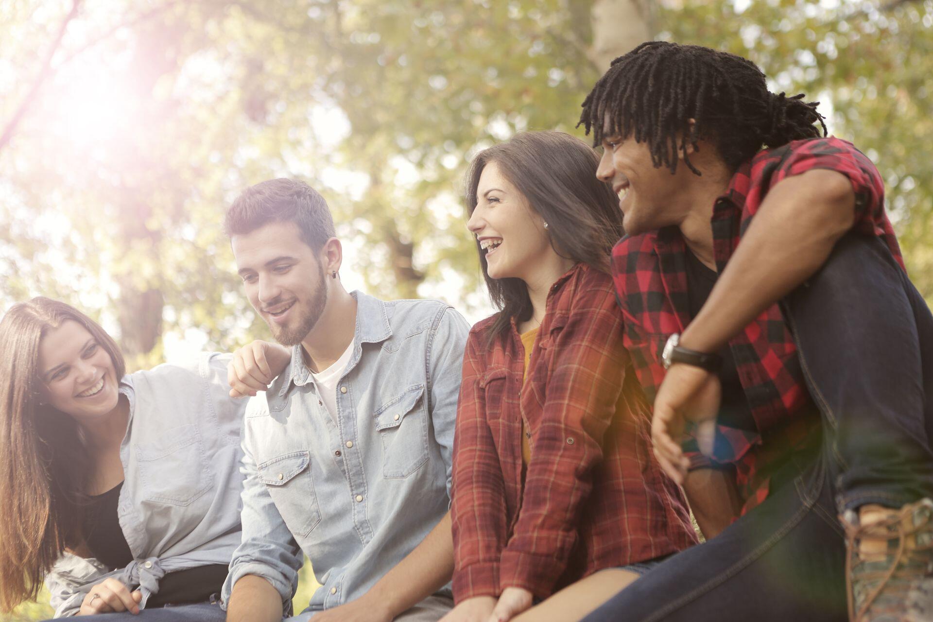 a group of four friends sitting on the grass outside, talking and laughing together