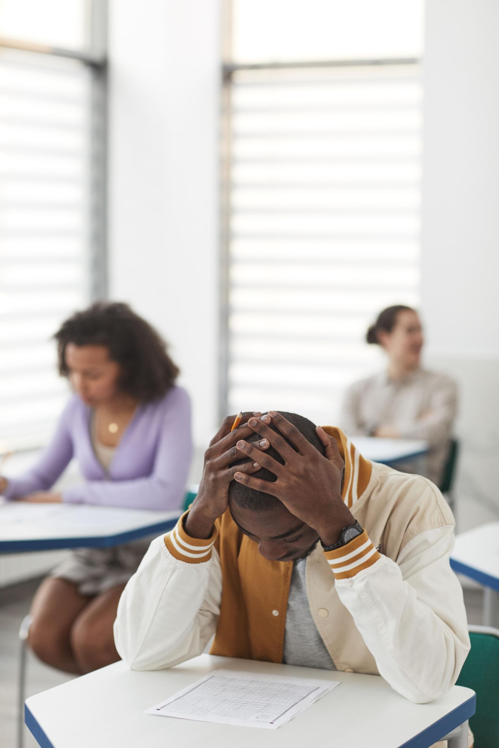 A student in a math class holds his head, visibly stressed.