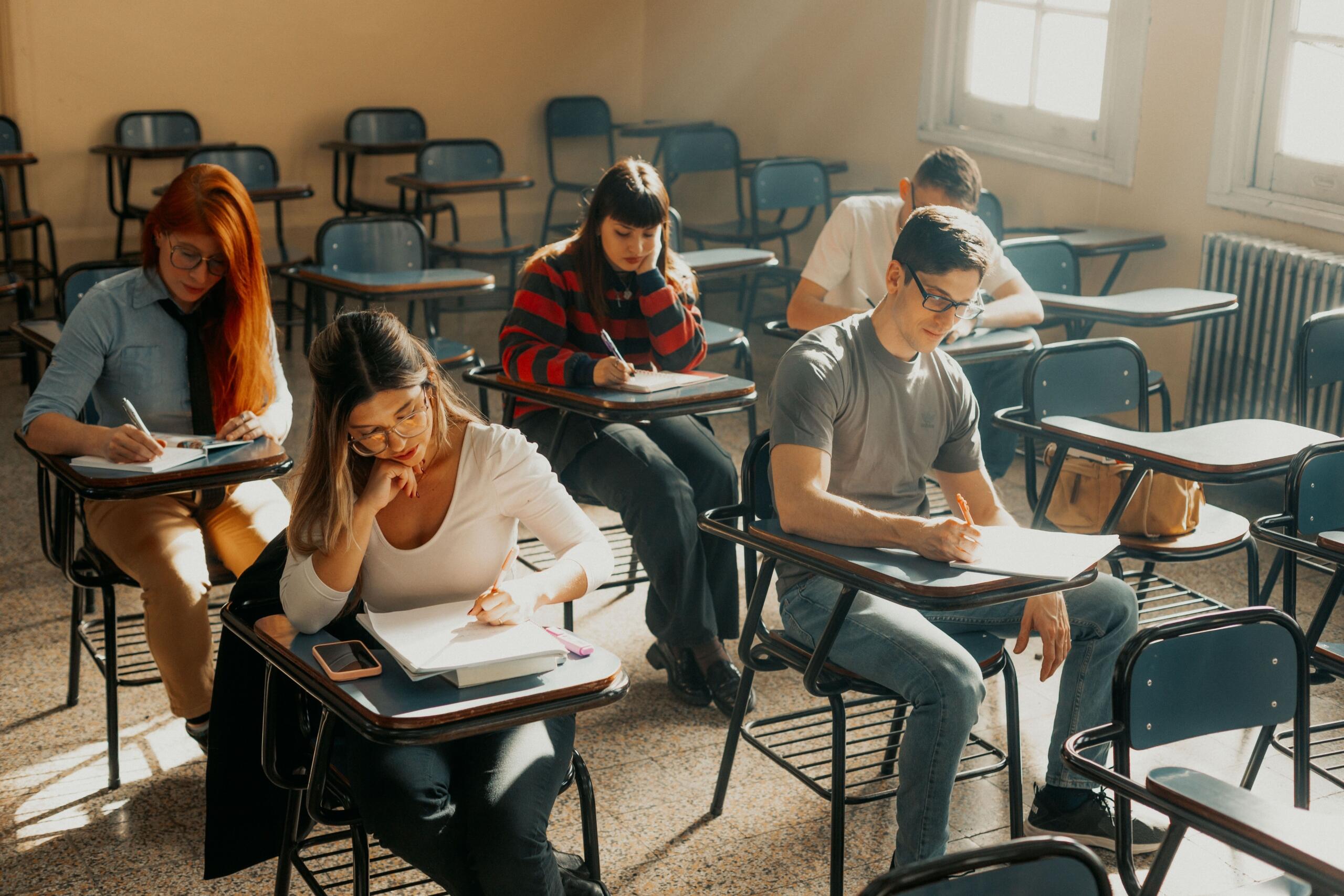 High school students write an exam in a classroom with sunlight streaming in.