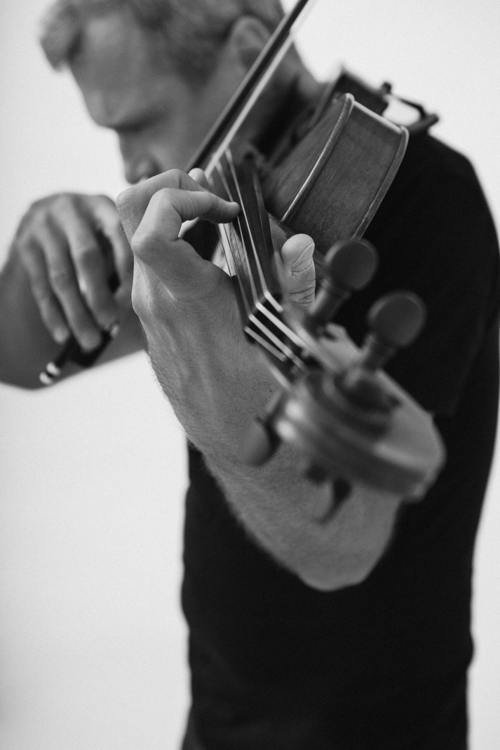 Black-and-white close-up of a musician playing a violin, with the bow crossing the strings.