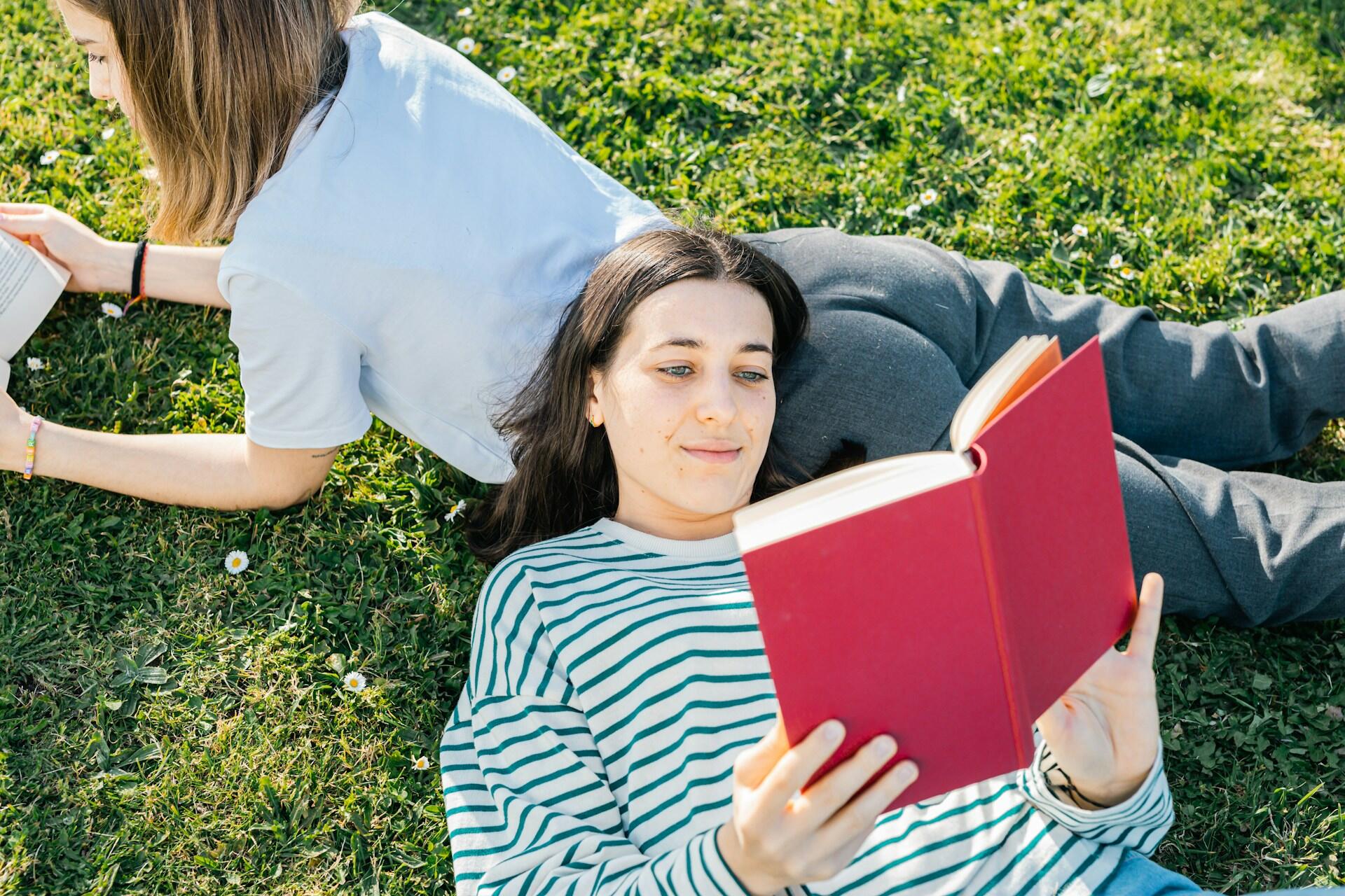 two people laying in the grass outside on a sunny day reading books