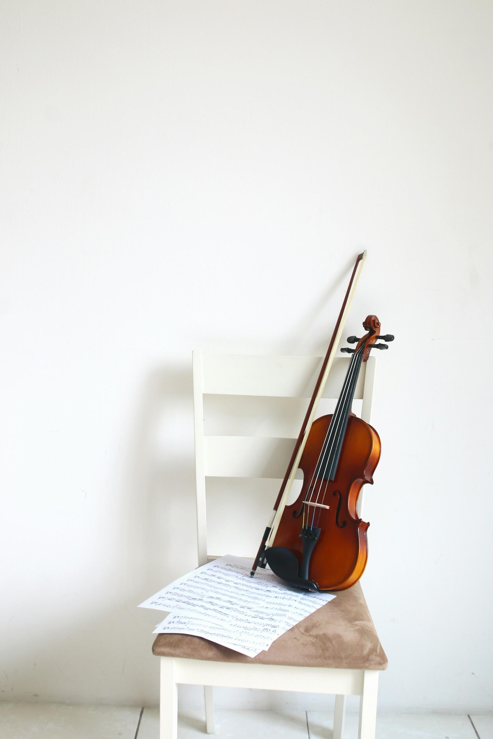 Violin and bow resting on a cushioned white chair beside sheets of music.