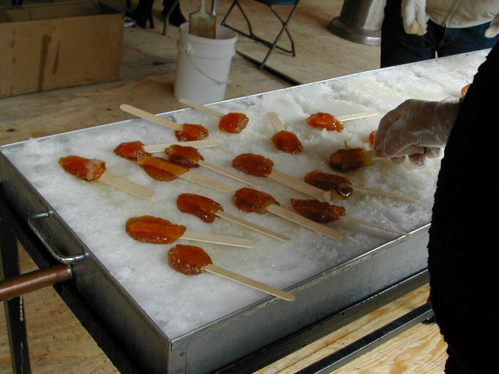 Maple taffy on sticks being poured and cooled on a bed of ice during a traditional maple syrup event.
