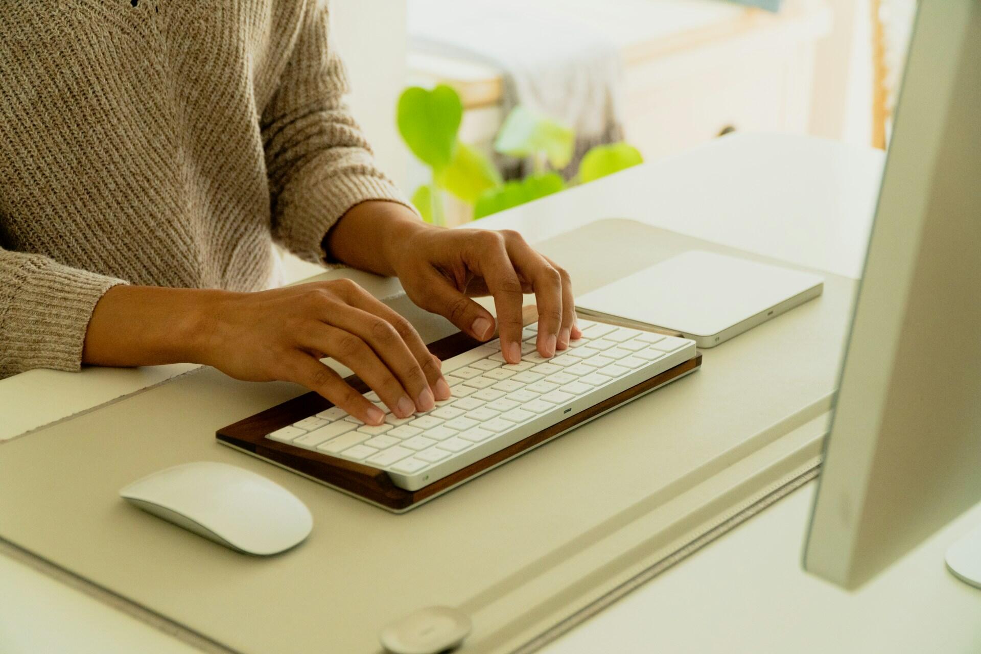 person typing on a keyboard for a desktop computer at a home desk