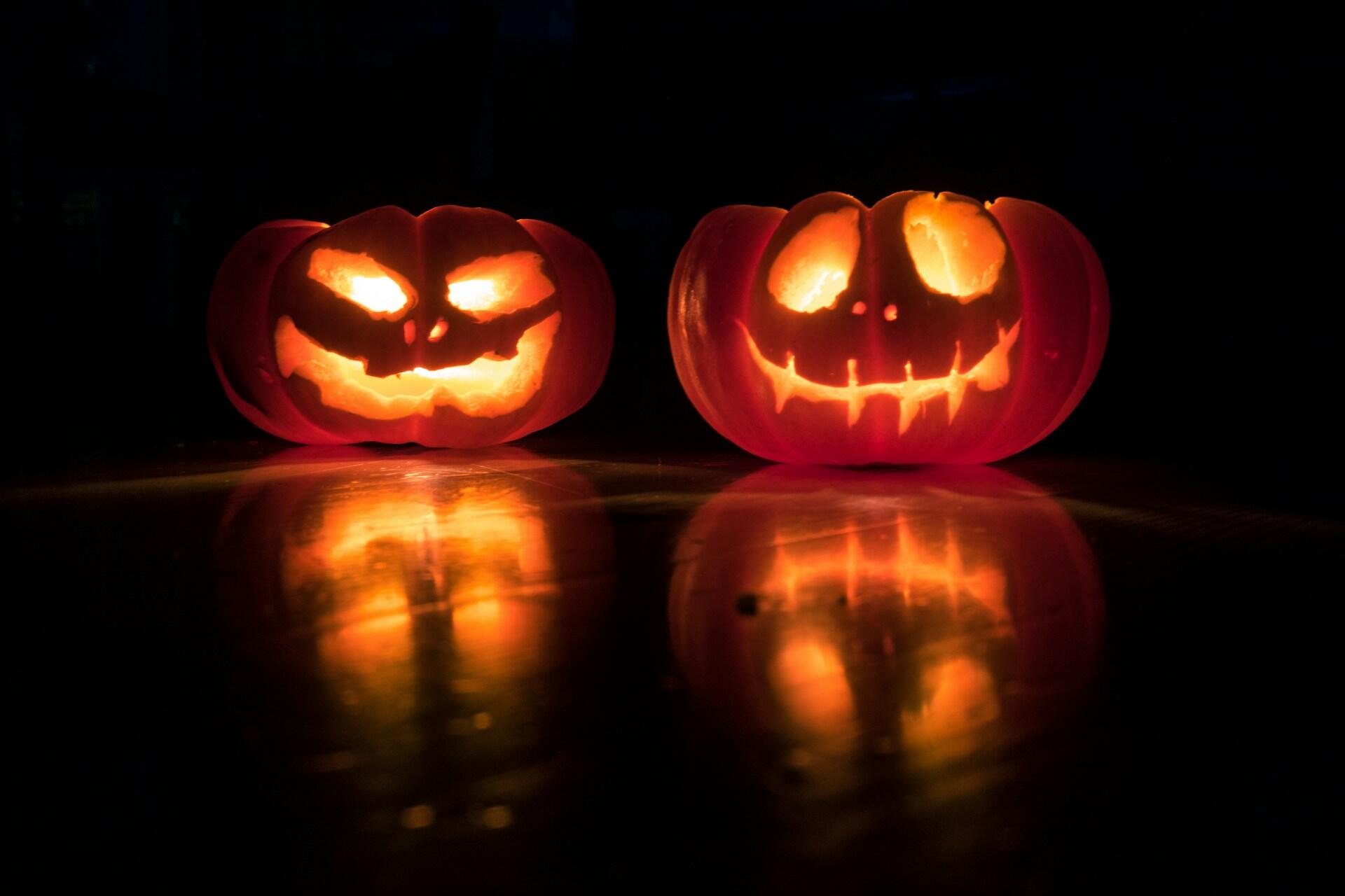 Two glowing jack-o'-lanterns with mischievous faces sit on a reflective surface against a dark background.