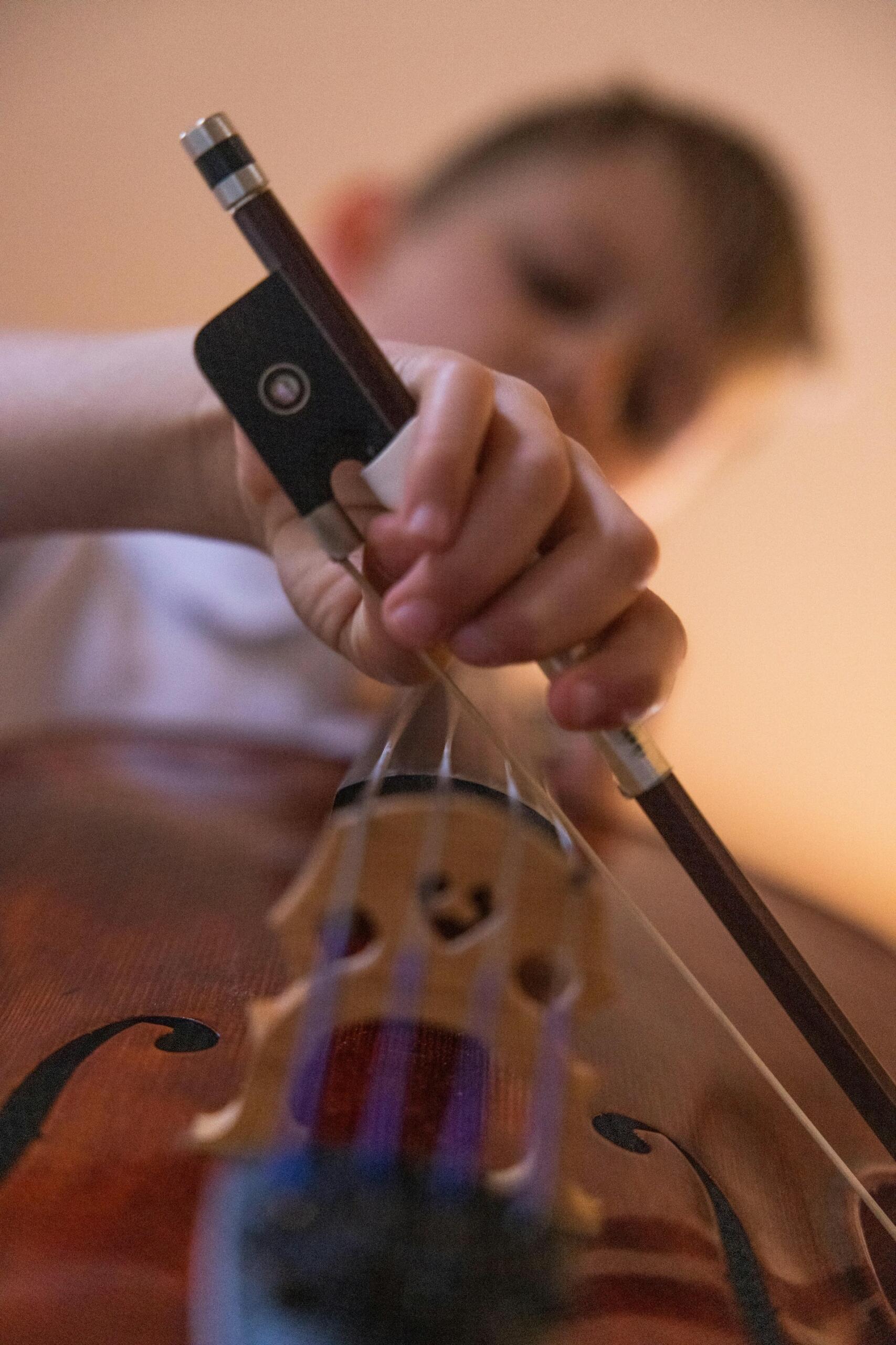 Close-up of a person playing a cello, with the bow and hand in focus.