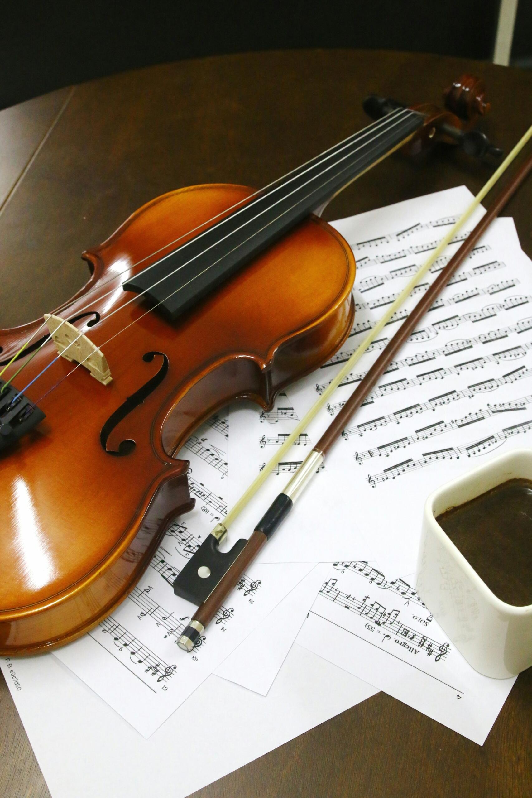 A violin and bow rest on printed sheet music beside a cup of coffee.