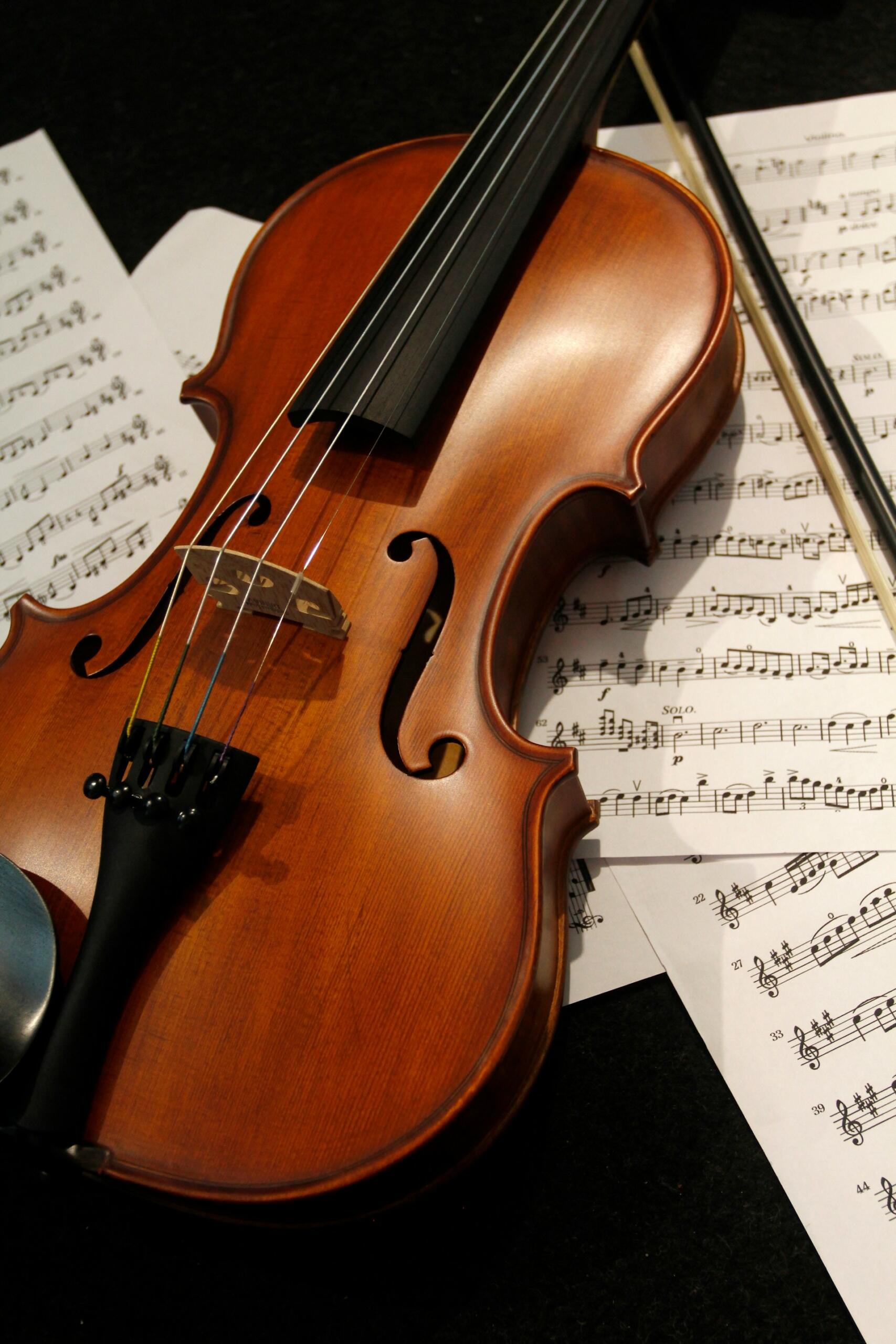 Close-up of a wooden violin and bow resting on printed sheet music.