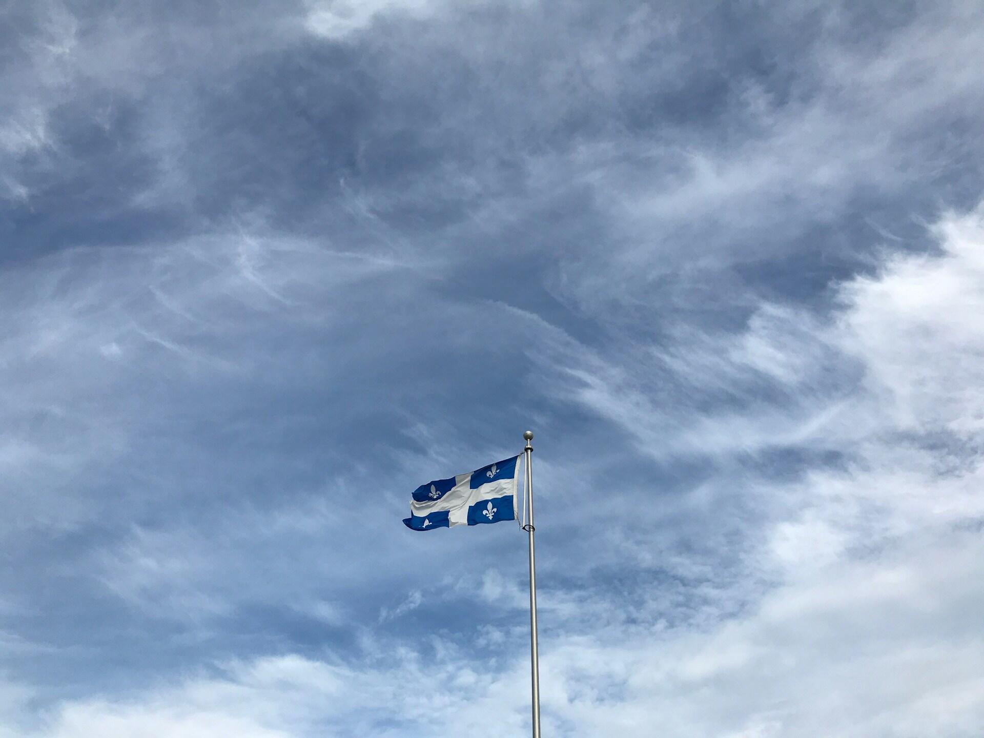 Quebec flag waving on a flagpole against a cloudy blue sky.