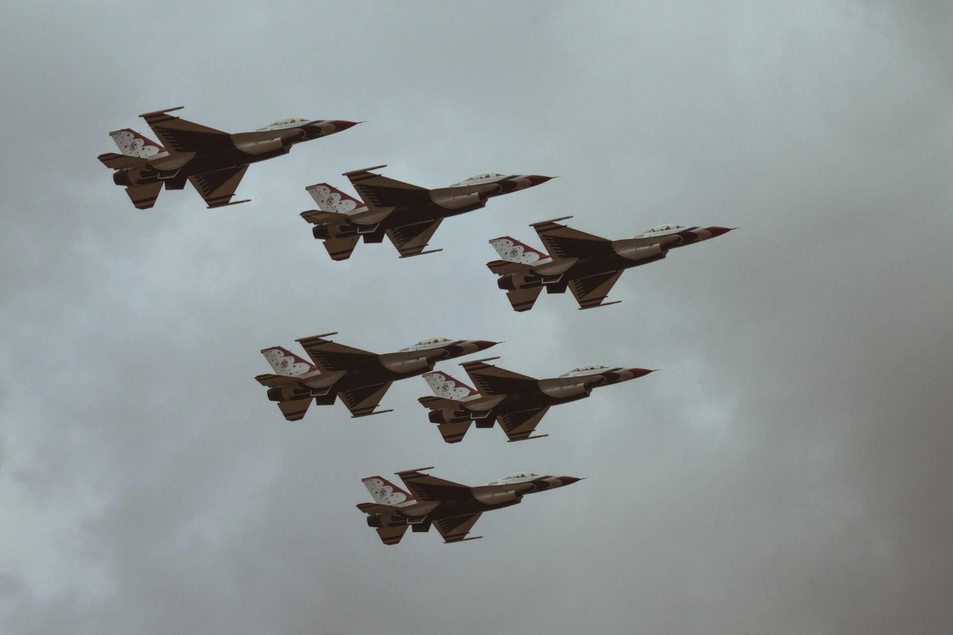 Six fighter jets fly in formation against a cloudy gray sky.