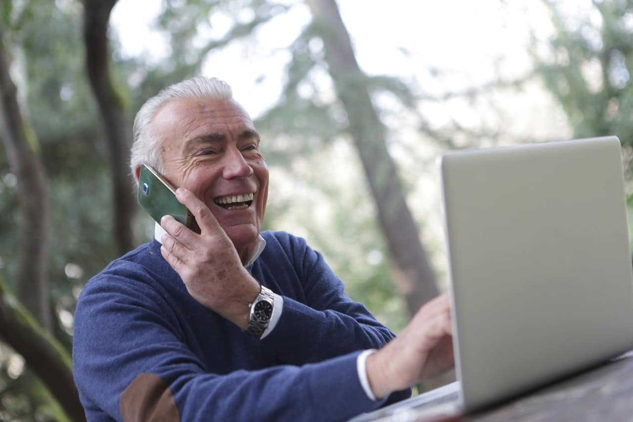 Vieil homme souriant avec son téléphone et son laptop