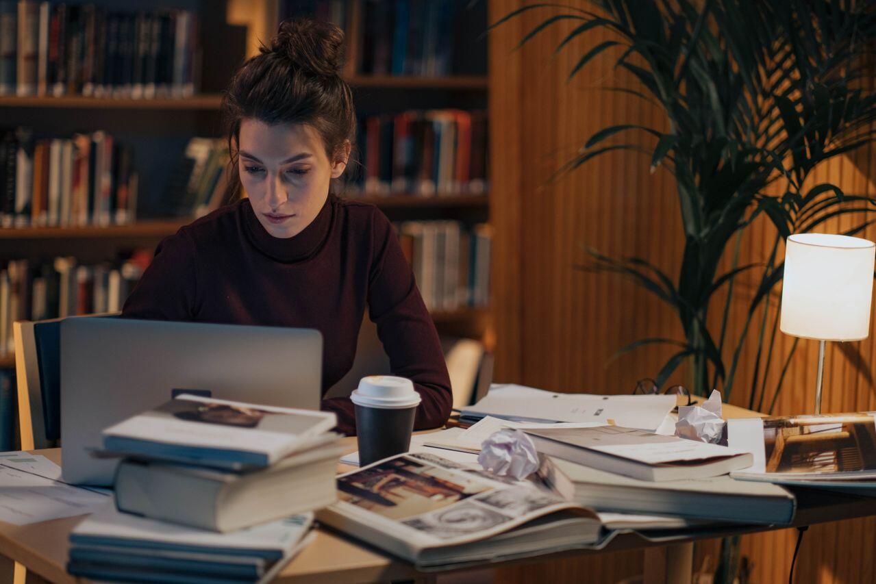 jeune femme dans la penombre etudiant a la bibliotheque avec ordi et cafe