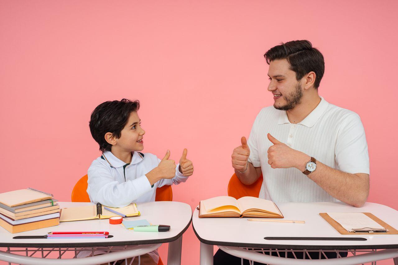 un homme et un petit garcon en classe sur fond rose levant les pouces en l air