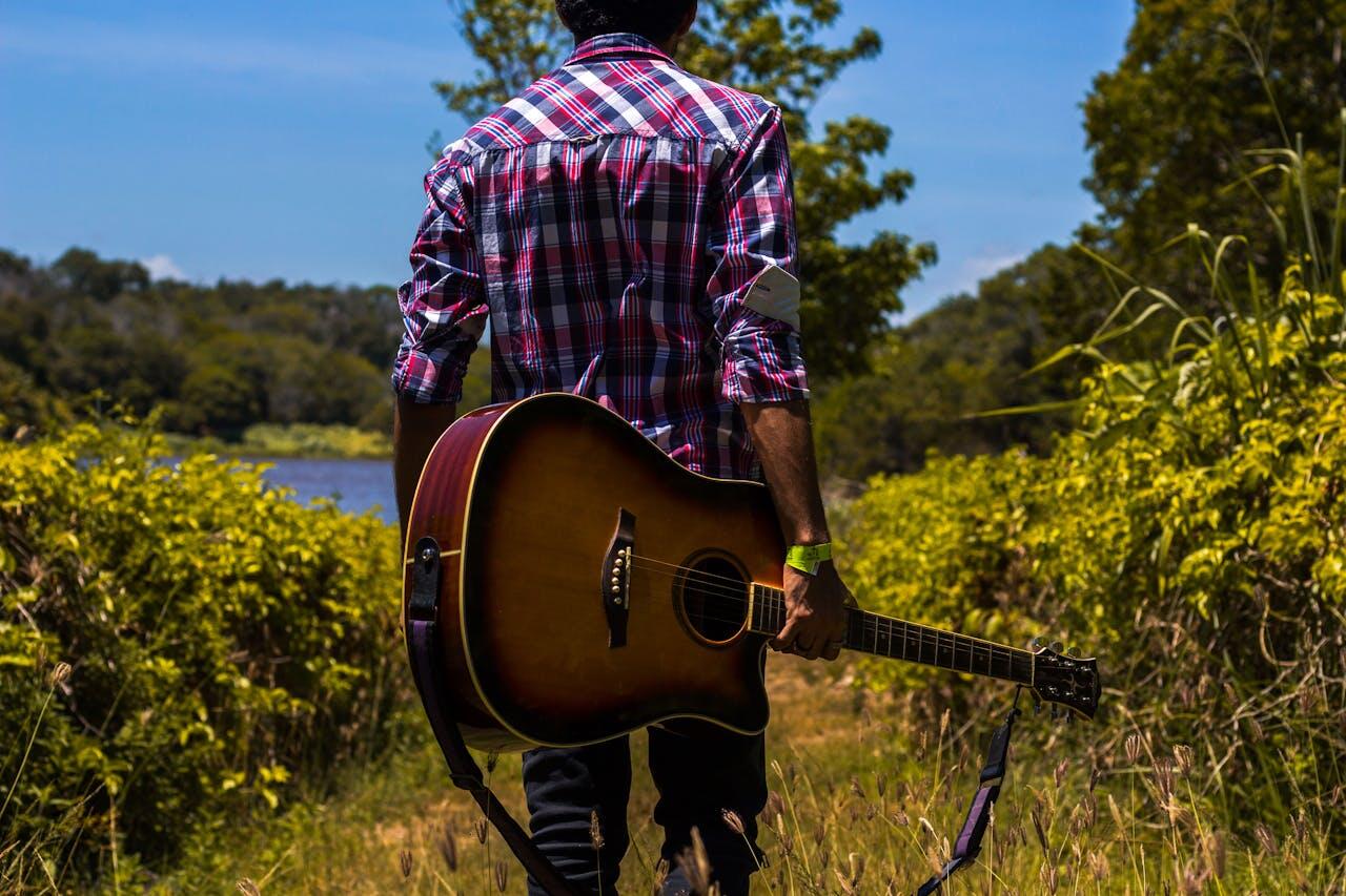 homme de dos avec sa guitare dans le paysage